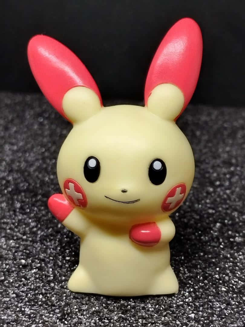 Plusle 行動玩偶 壁紙 — 一個快樂的黃色比卡超公仔，有紅色耳朵和臉頰，站在深色紋理表面上。