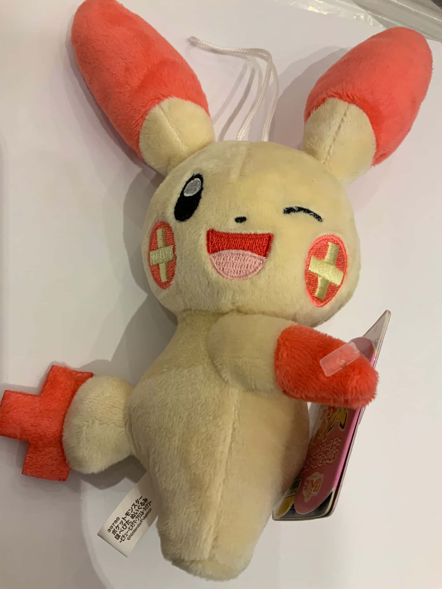 一個微笑眨眼的毛絨玩具，有橙色耳朵和十字補丁。