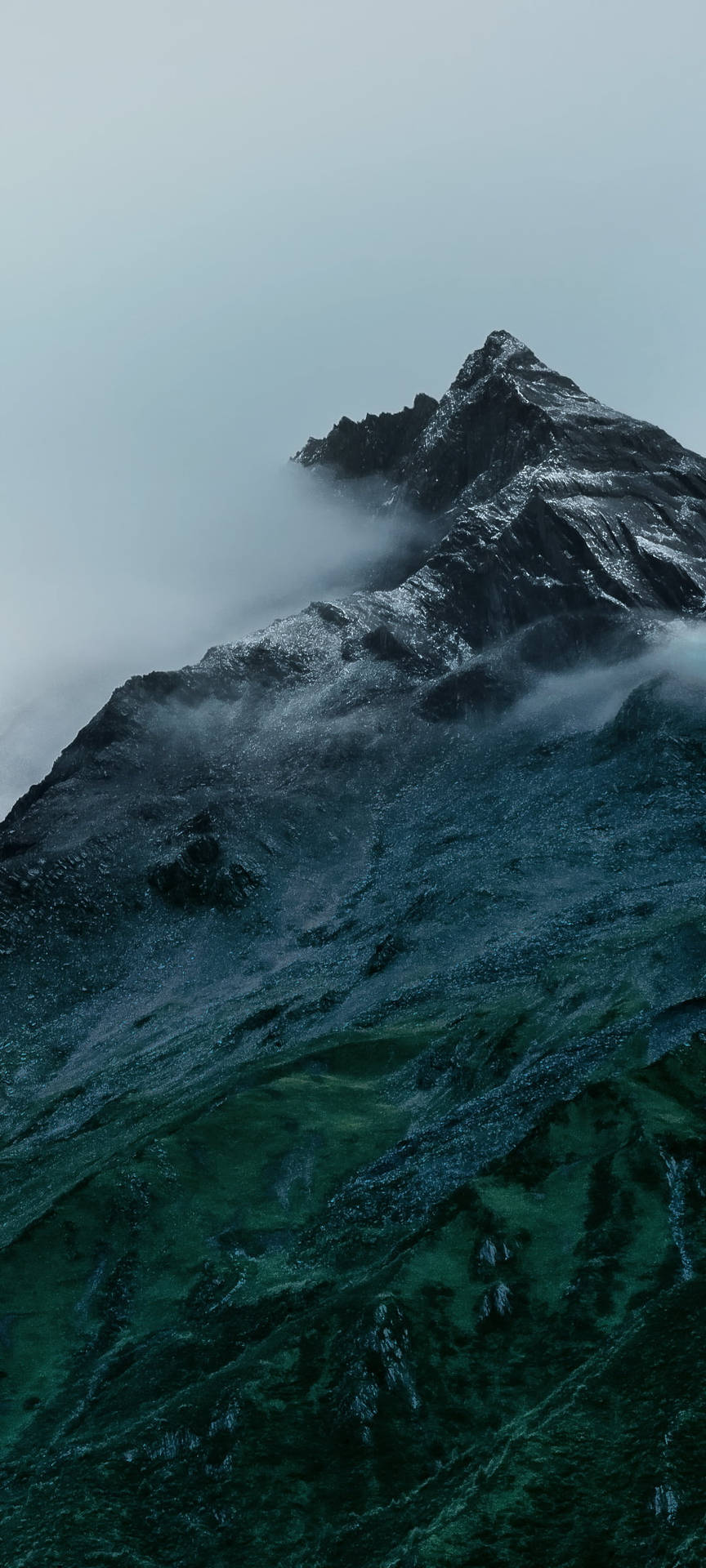 一座積雪的山峰穿過薄霧升起，下方是綠色的山坡。