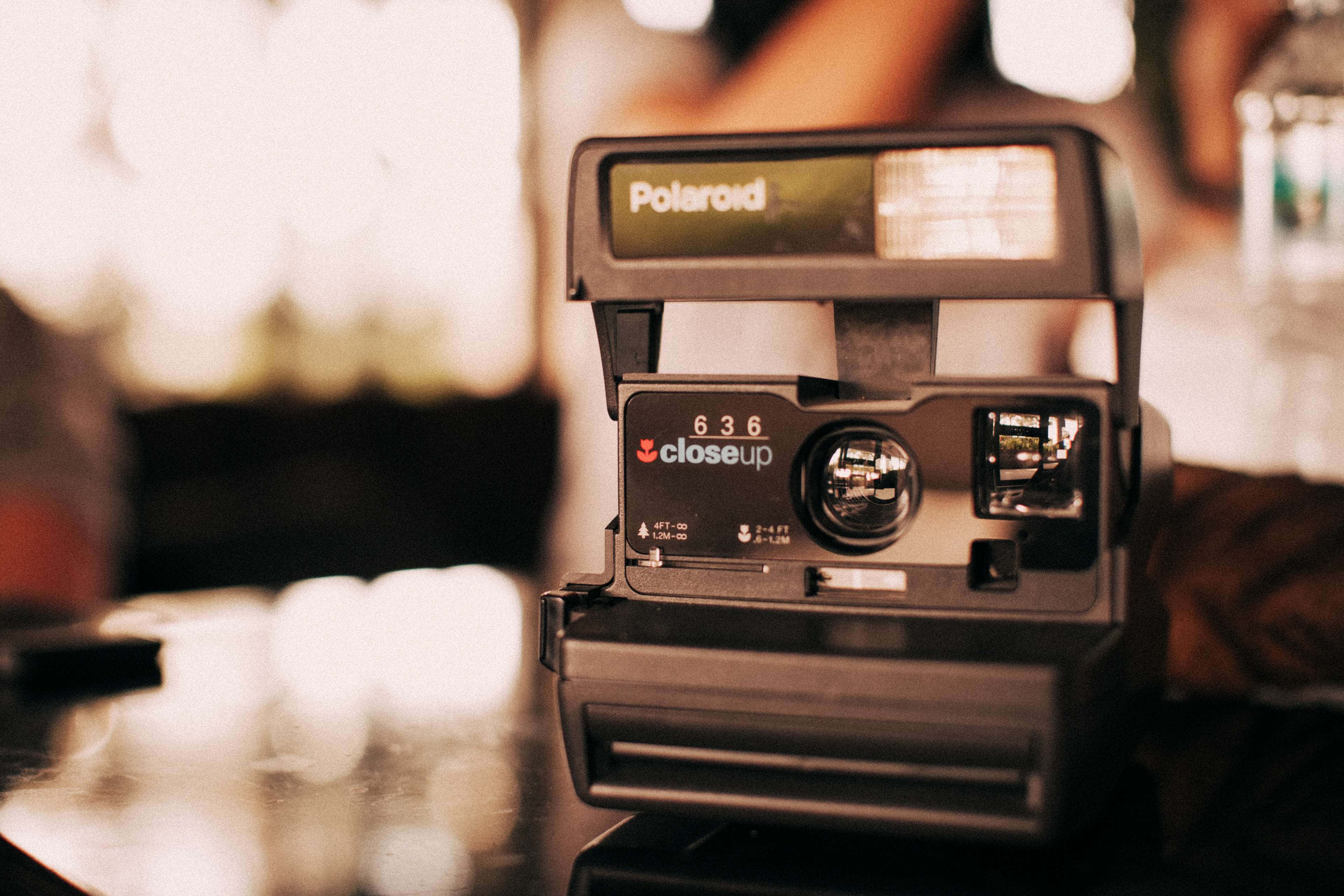 經典Polaroid相機的永恆復古魅力 壁紙 — 一部復古Polaroid 636 Closeup相機放在反射表面上，沐浴在溫暖的金色光線中，背景柔和模糊。