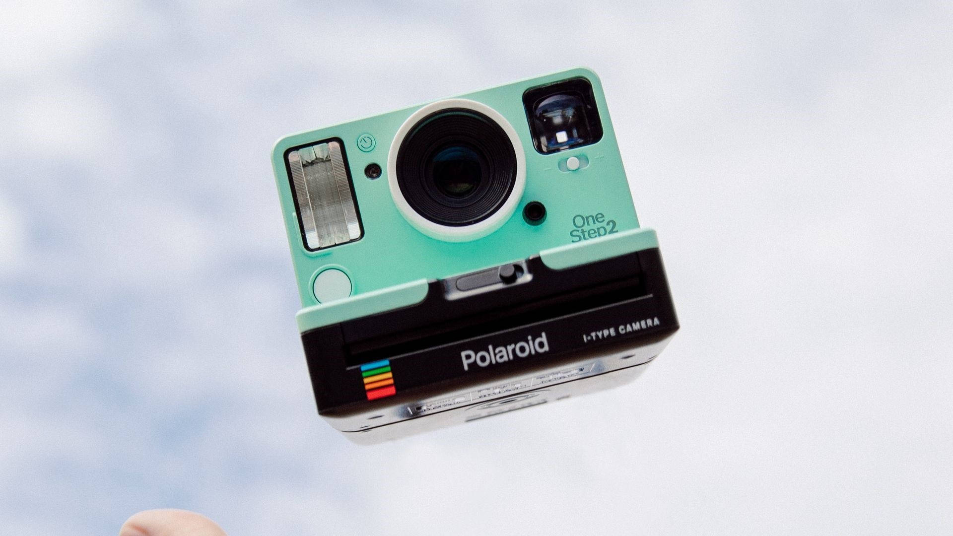 一部薄荷綠色的Polaroid相機漂浮在雲天前。