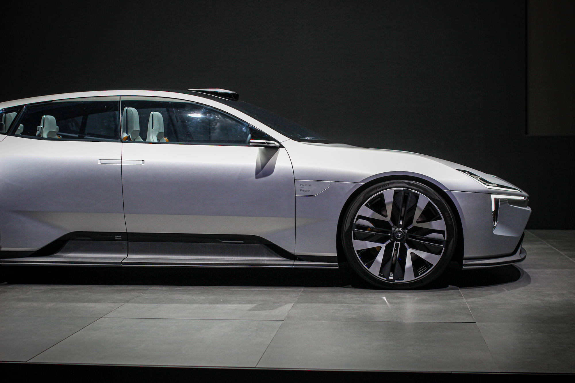 Polestar 2緊湊型車 壁紙 — 一輛時尚的銀色未來感汽車，帶有黑色飾邊和發光頭燈，在工作室燈光下展示在深色瓷磚地板上。