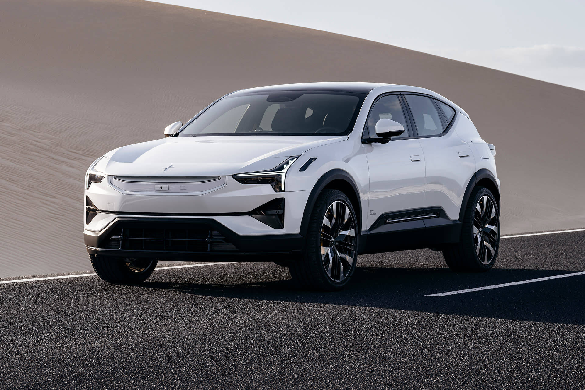 Polestar 3電動SUV 全貌 壁紙 — 一輛時尚的白色電動SUV在明亮的日光下，以簡約的米色沙丘為背景，行駛在鋪砌的道路上。