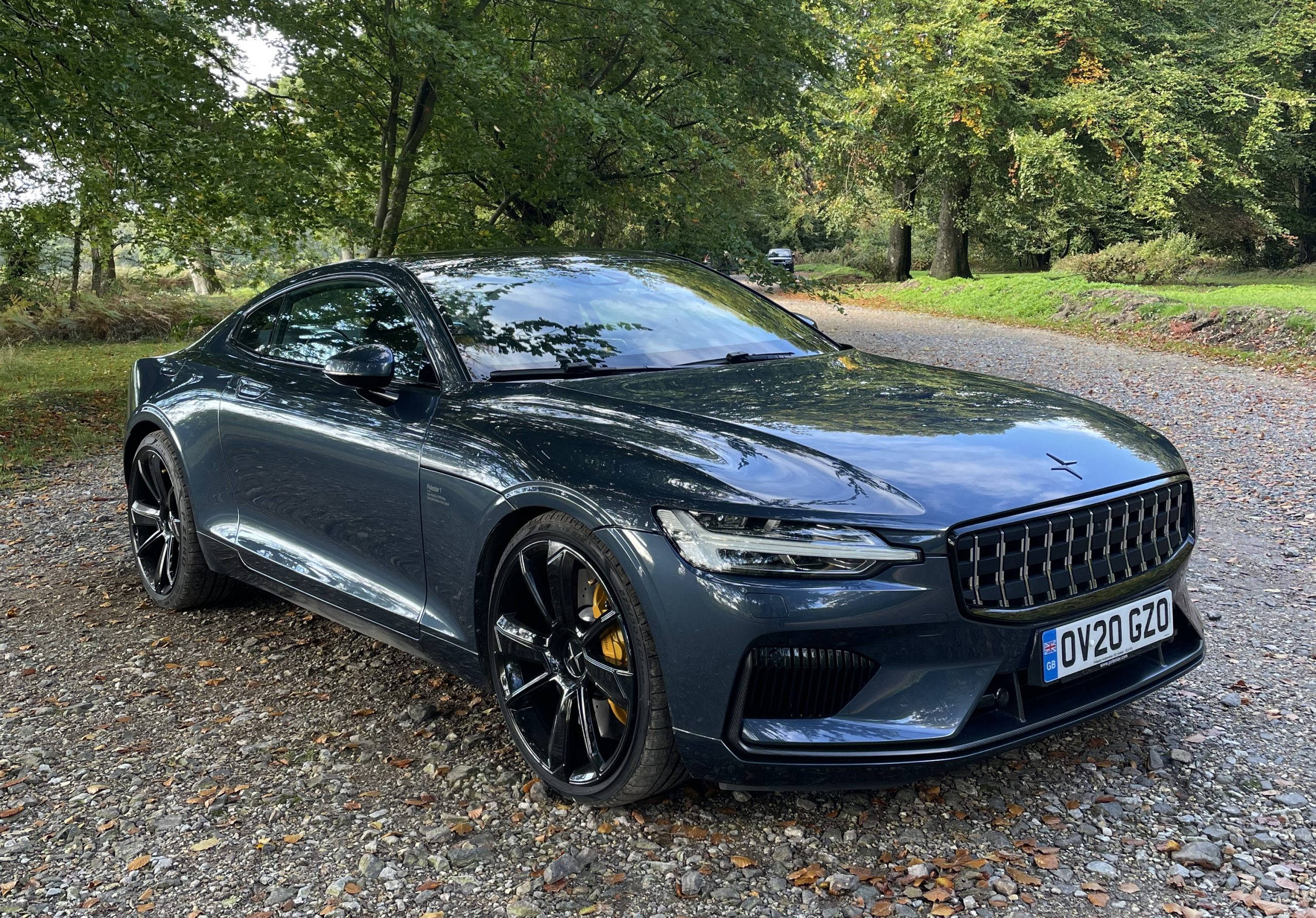 Polestar車輛停泊於當地公園 壁紙 — 一輛時尚的深灰色Polestar 2電動車停泊在碎石路上，周圍環繞著茂密的綠樹。