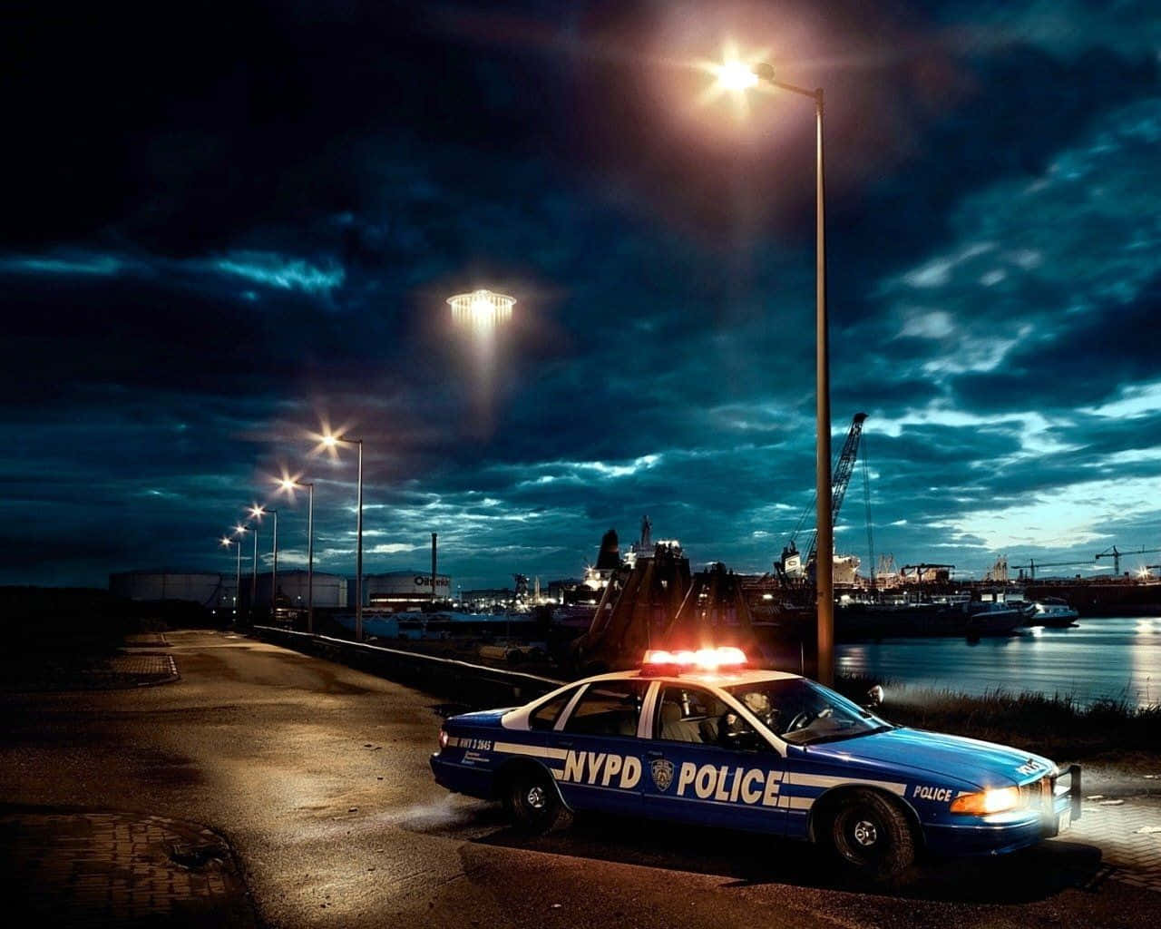 NYPD警車夜間停在海濱碼頭，有街燈和烏雲。