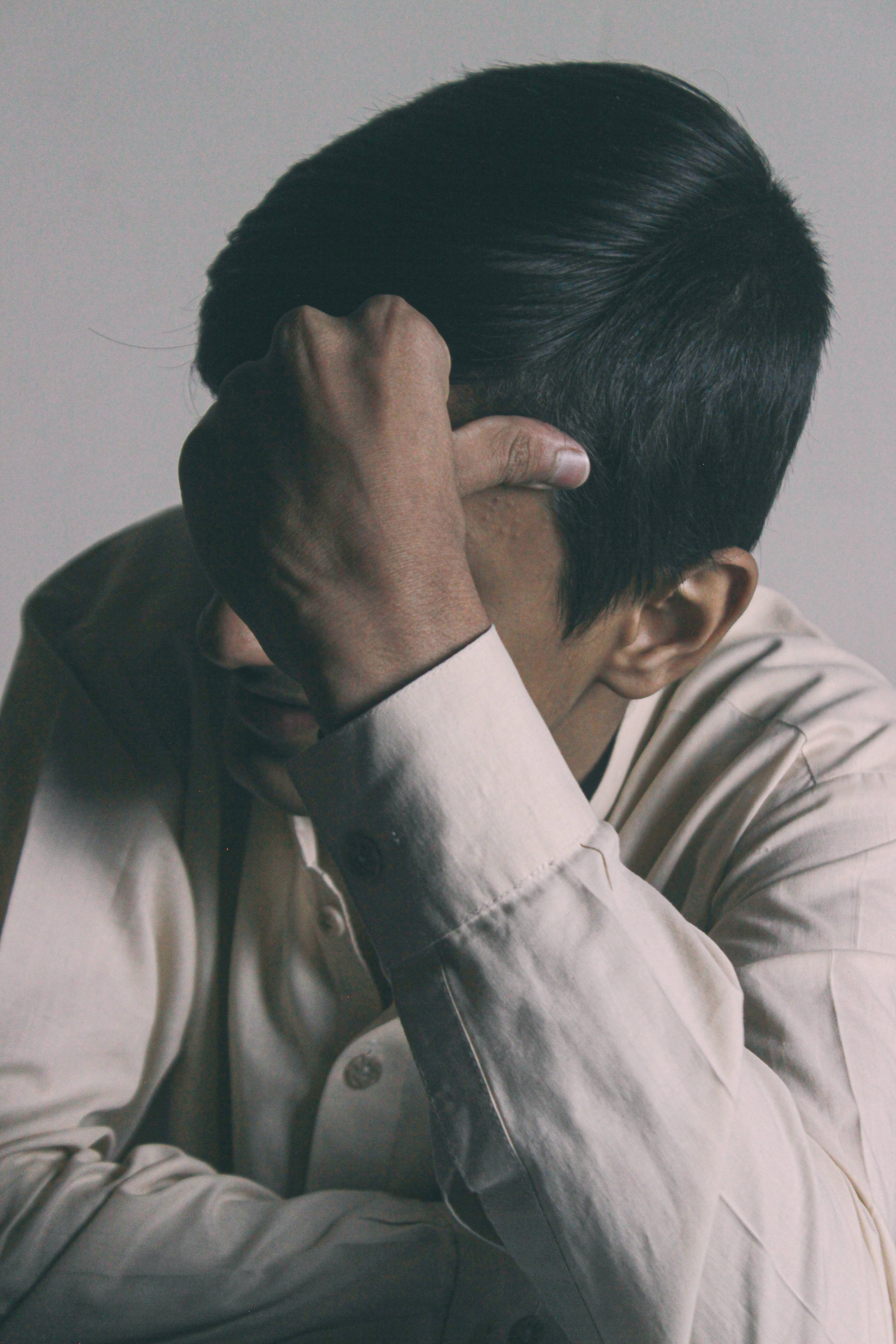 憂鬱男孩長袖Polo衫 壁紙 — 一個穿著淺色襯衫嘅人用一隻手遮住塊面，背景係純色。