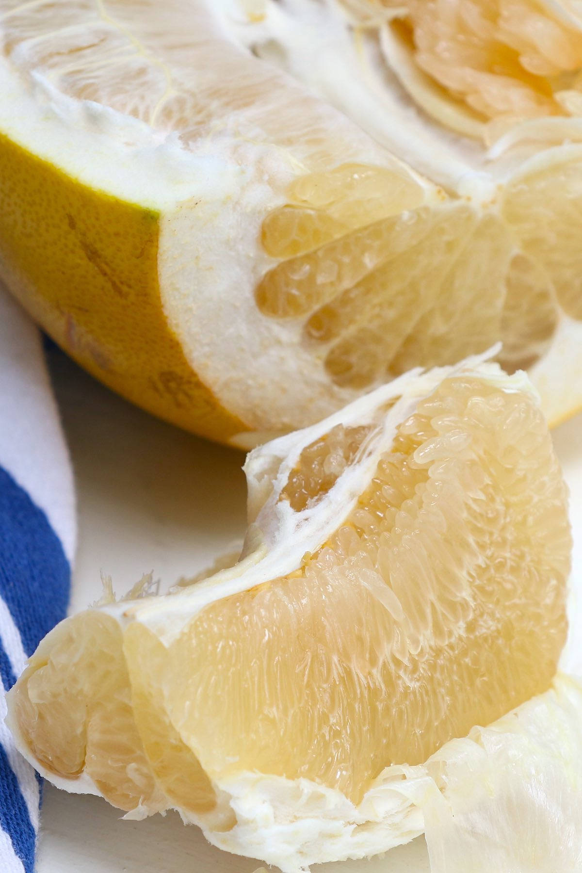 pomelo 果片 壁紙 — 一個特寫鏡頭，多汁的淡黃色柚子瓣連同白色海綿層，放在藍白條紋布上，旁邊是半個柚子。