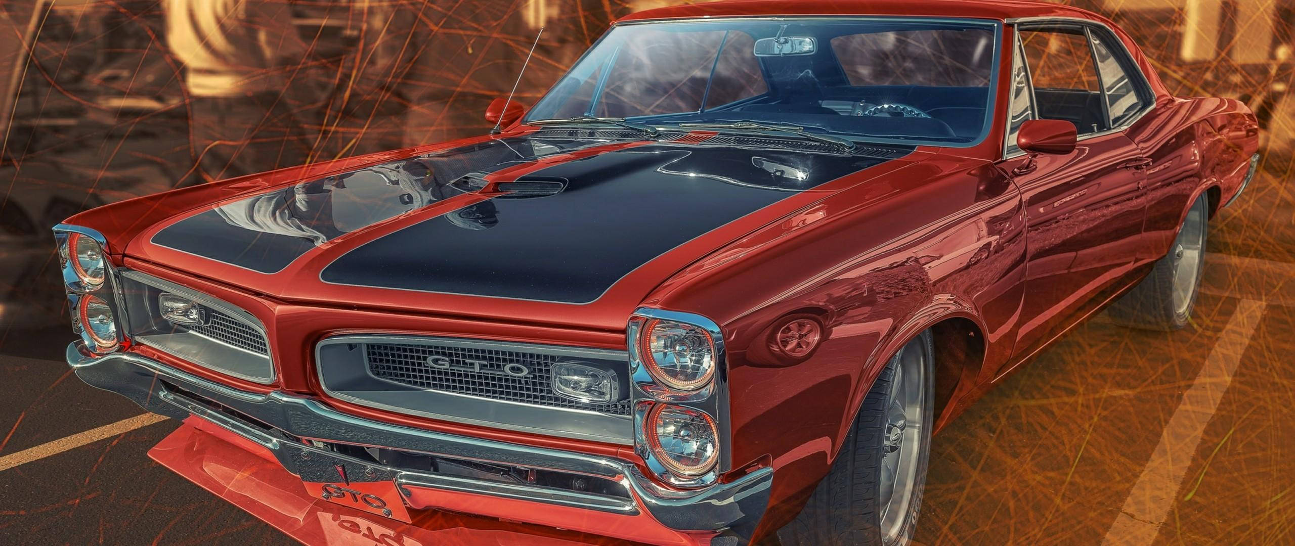 Pontiac GTO 古董車 壁紙 — 一輛光澤的紅色經典肌肉車，帶有黑色引擎蓋條紋，在溫暖的金色燈光下閃耀，背景是火熱的抽象圖案。