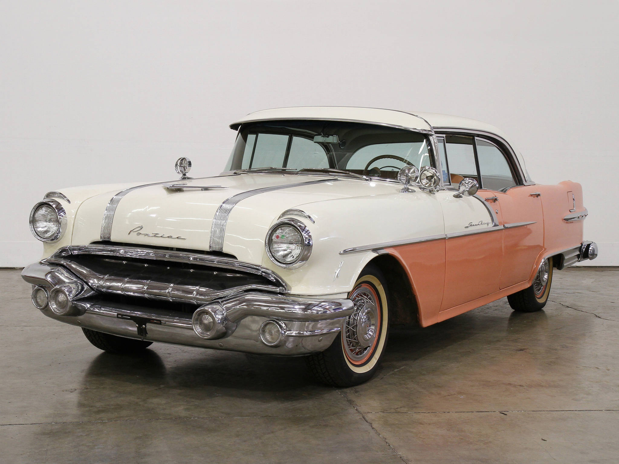 精緻修復 Pontiac Star Chief 壁紙 — 一輛1950年代復古龐蒂亞克轎車，奶油色和珊瑚色車漆在簡約車庫的攝影棚燈光下閃閃發光。