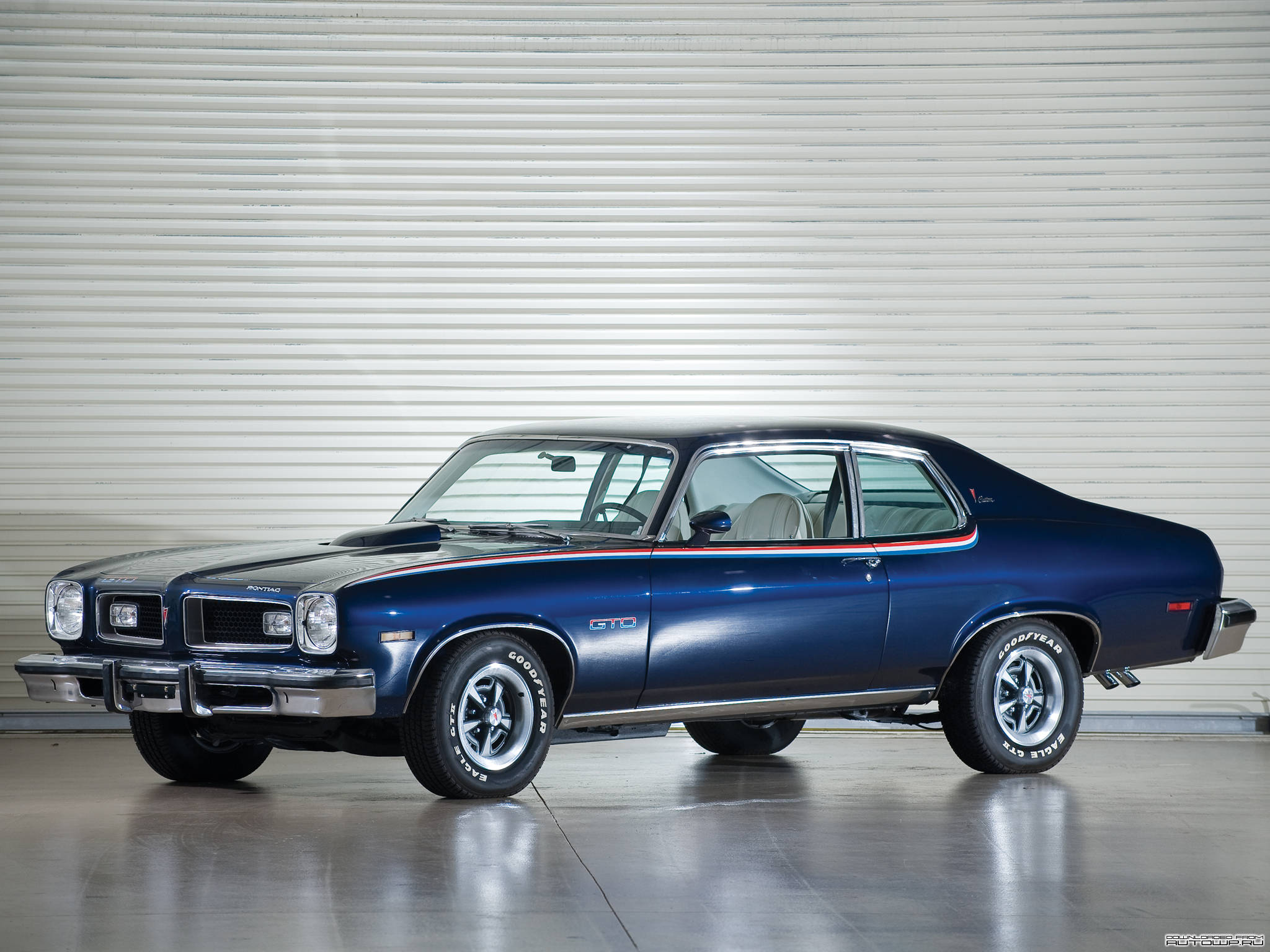 藍色 Pontiac Ventura 壁紙 — 一架時尚的藍色經典肌肉車，帶有紅、白、藍條紋，停放在一個乾淨的車庫裡，後面是波紋金屬牆。
