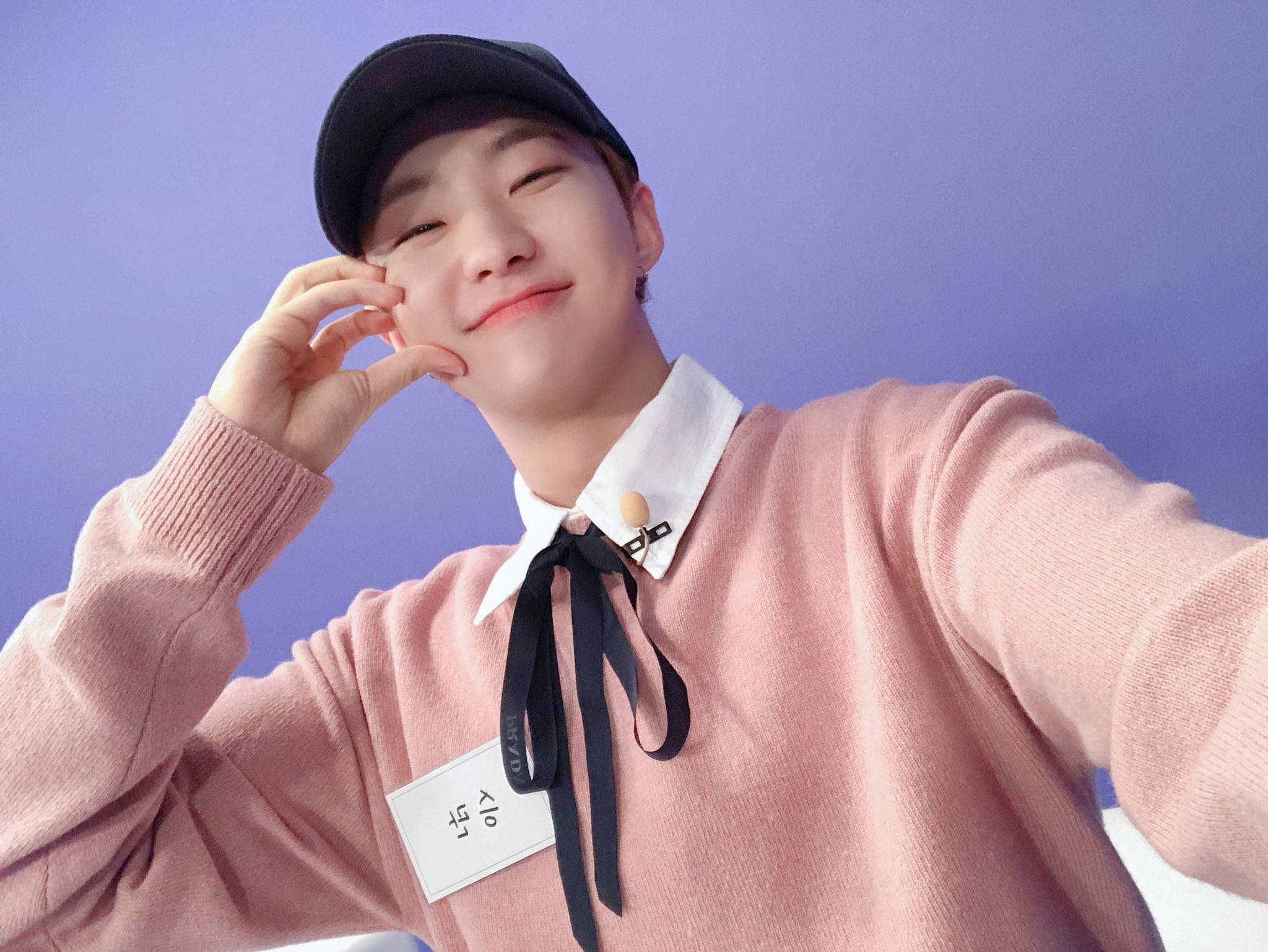 Pop Idol 節目 - Hoshi 來自 Going Seventeen 壁紙 — 一位穿著粉紅色毛衣和黑色帽子的年輕人，在純紫色背景前微笑自拍。