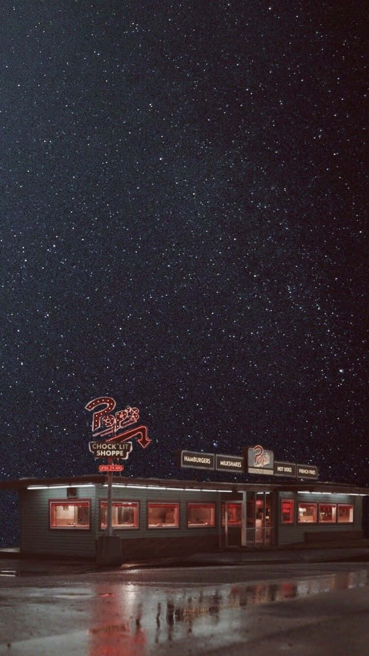 Pop's 餐廳夜景亮麗 iPhone 壁紙 — 星空下嘅復古餐廳，濕漉漉嘅路面反射住霓虹燈光。