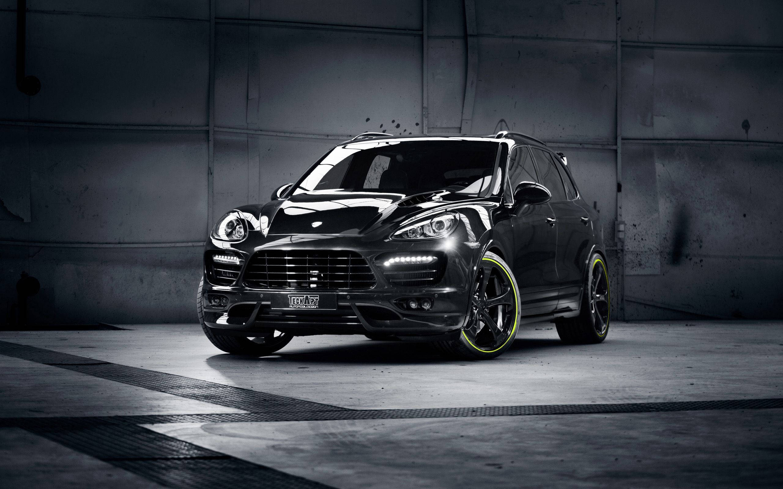 Porsche Cayenne Jeep 壁紙 — 一輛時尚的黑色保時捷Cayenne配備螢光黃輪圈，在戲劇性燈光下停泊在粗糙的混凝土車庫中。