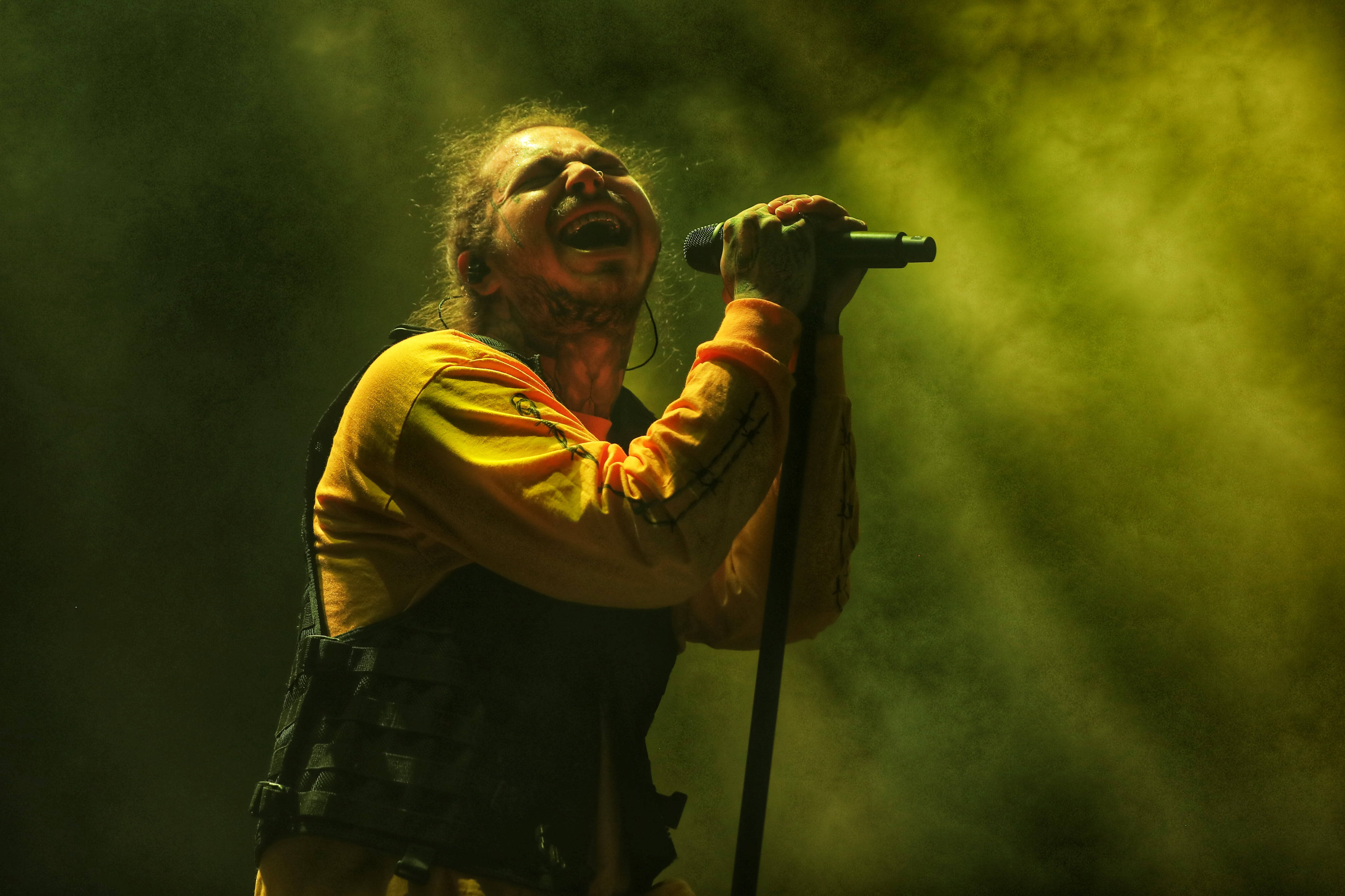 Post Malone 2018波特蘭演唱會 壁紙 — 一位充滿熱情的歌手在強烈的黃色舞台燈光和旋轉的煙霧中對著麥克風高歌。