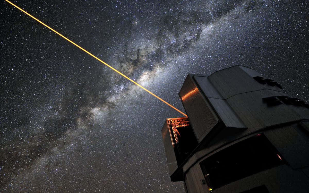  壁紙 — 一道強大的黃色激光束從望遠鏡射向佈滿銀河的星空夜空。