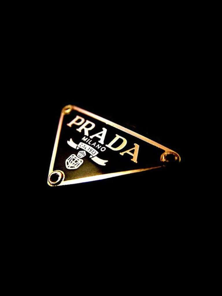 Prada經典系列的優雅展覽 壁紙 — 金色Prada三角形標誌胸針在戲劇性燈光下於純黑背景上閃耀。