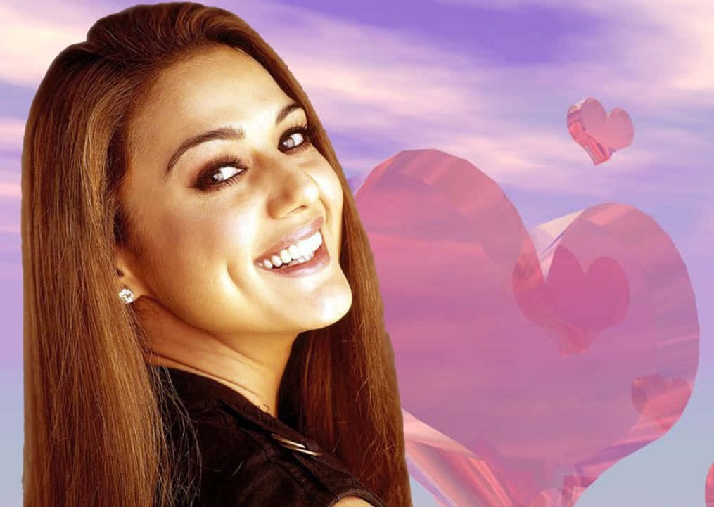 Preity Zinta 微笑紅心背景 壁紙 — 一位微笑的長棕髮女性，背景是夢幻的紫色天空，漂浮著粉紅色水晶心形。
