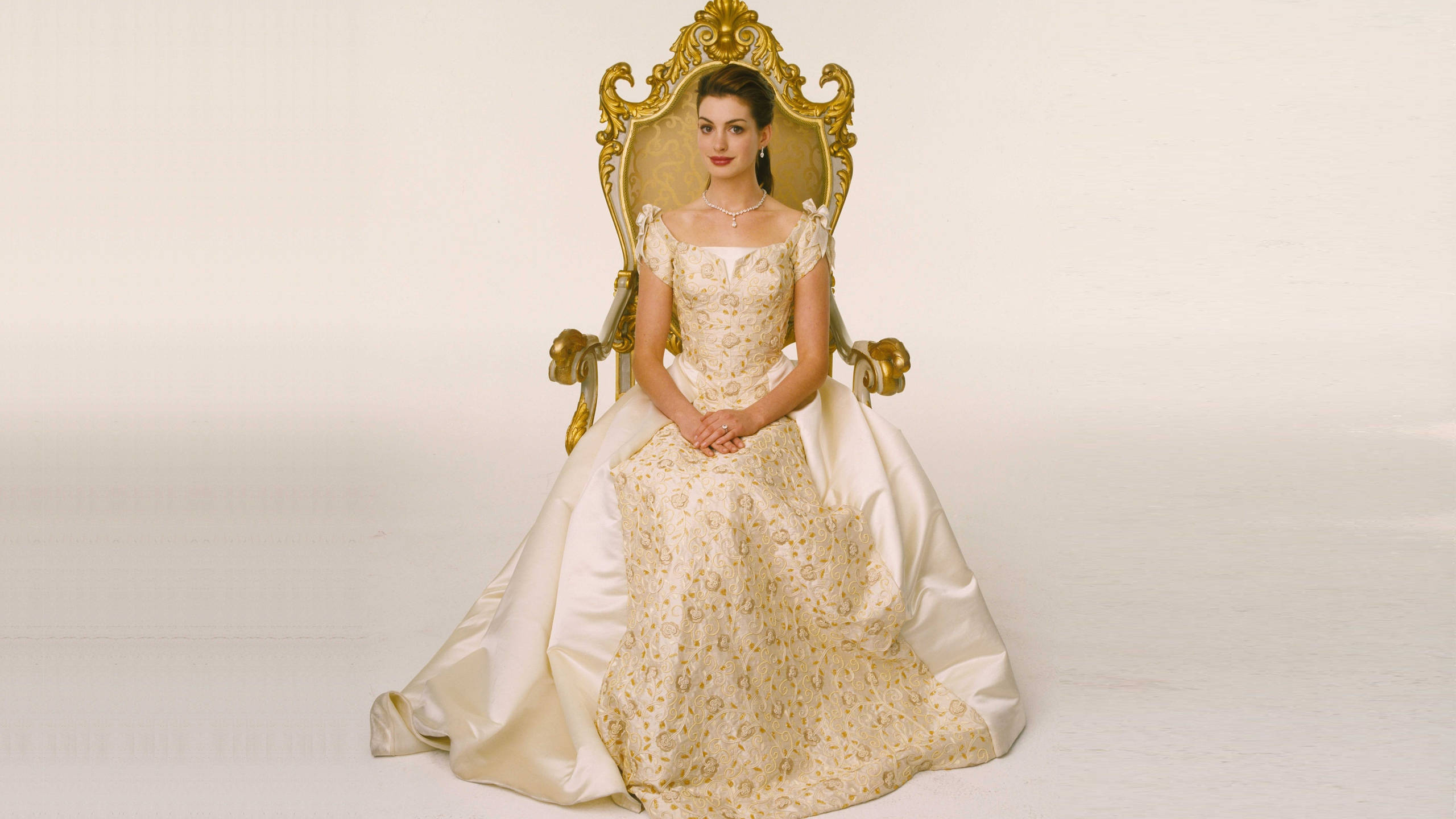 Princess Mia 加冕禮服 壁紙 — 一位身穿華麗金色和奶油色長袍的女性，端莊地坐在鍍金寶座上，背景是純白色。