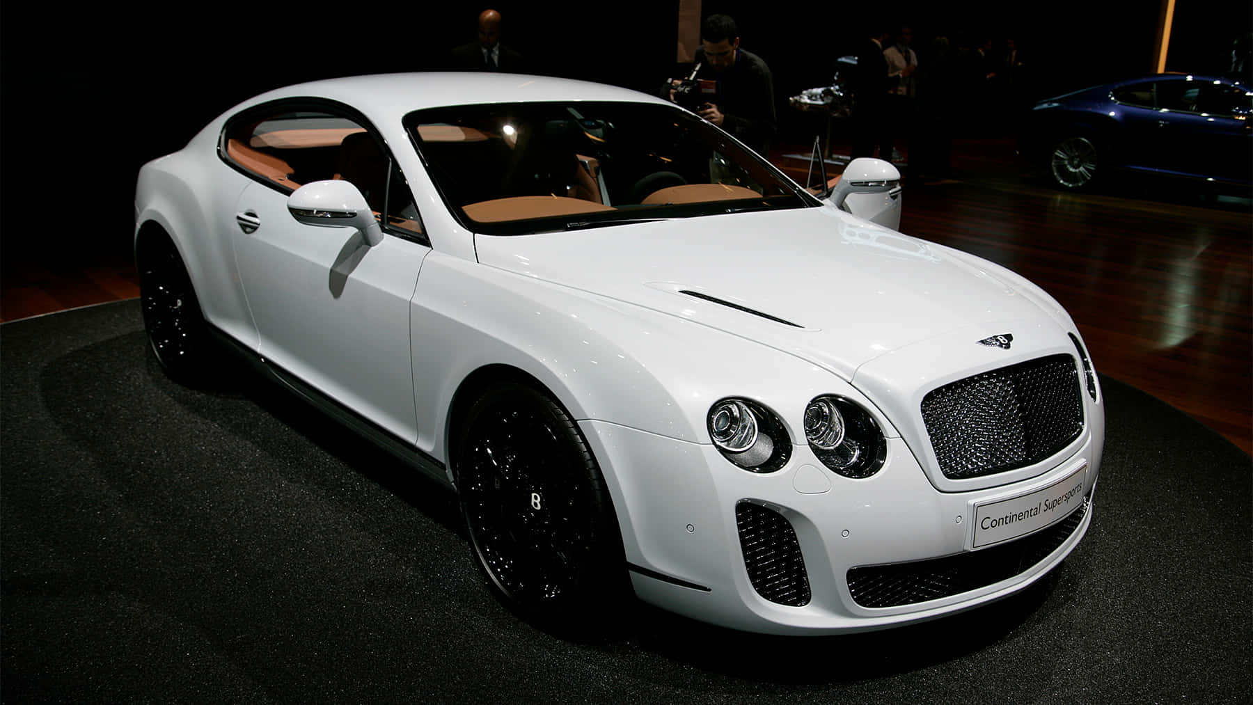 Bentley Continental Supersports 桌布 壁紙 — 一輛純白色的賓利 Continental Supersports 在展覽燈光下閃閃發光，配備黑色輪圈和米色內飾。