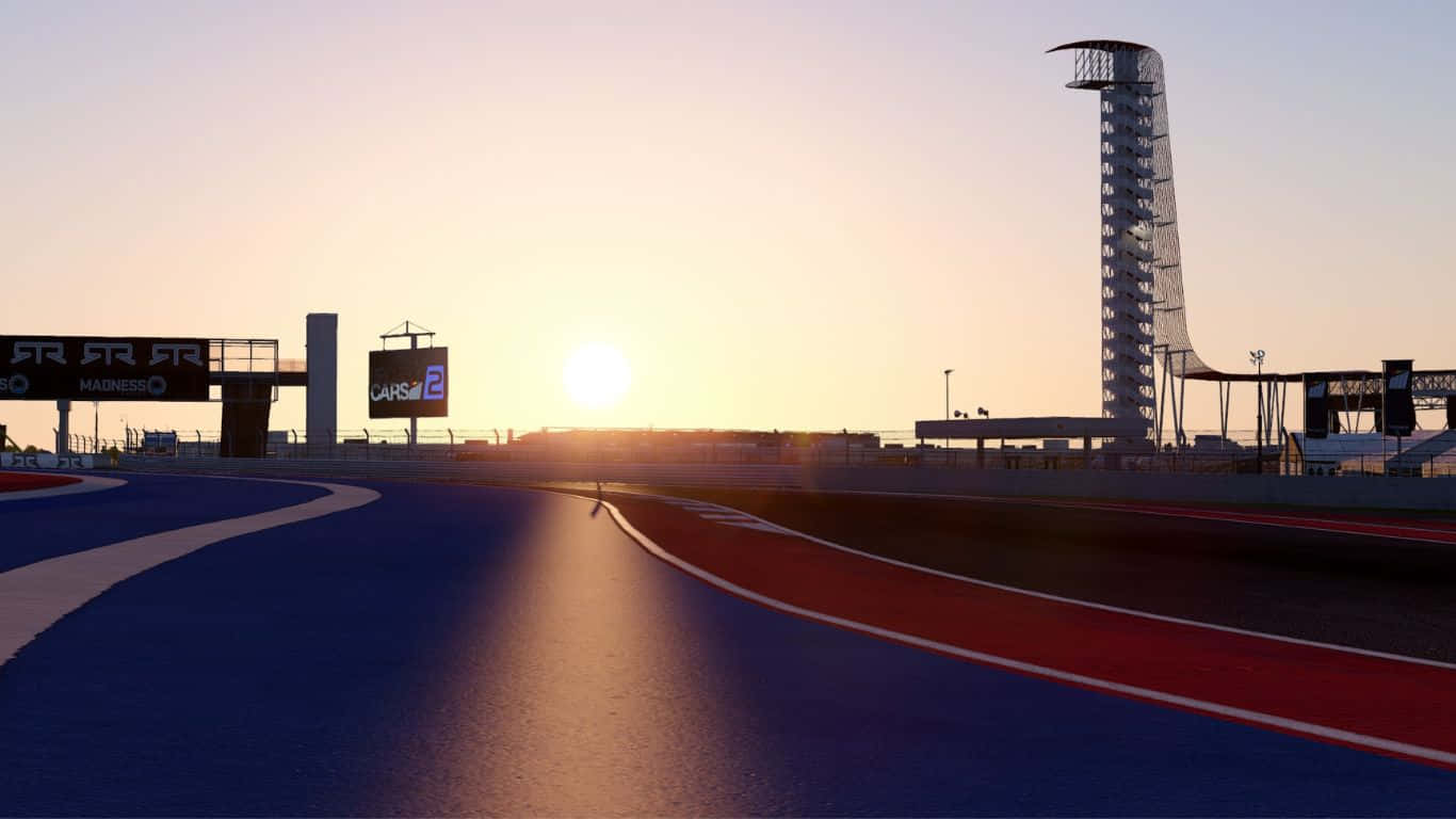 Project Cars 2 美國美洲賽道背景 壁紙 — 夕陽在時尚的藍紅賽道上閃耀，現代塔樓和標誌在天空的映襯下形成剪影。