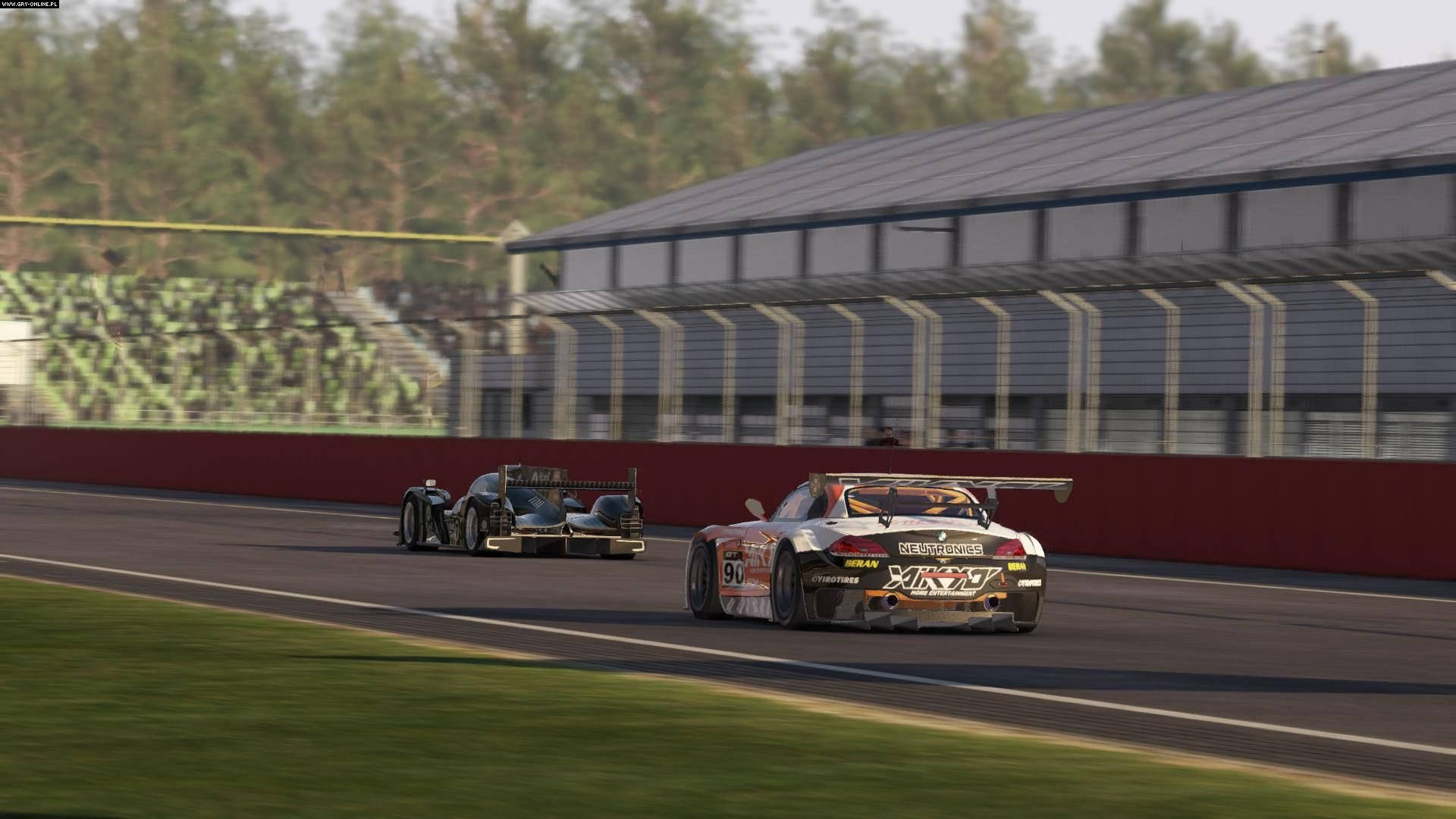 Project Cars 4K 宝马拉力賽車 壁紙 — 兩輛賽車在陽光明媚的賽道上並排飛馳，背景有看台和樹木。