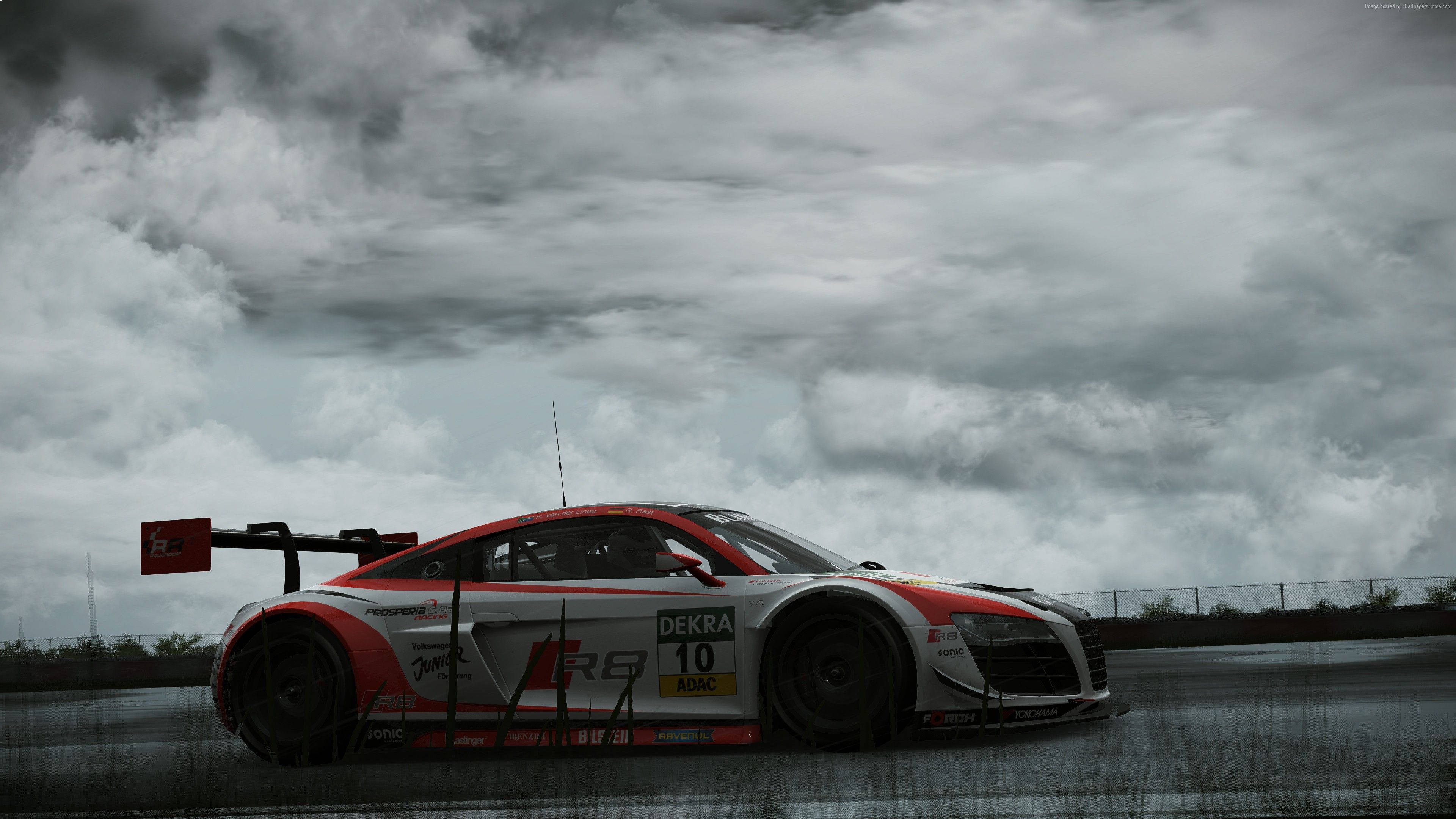 Project Cars 4K 奧迪 R8 LMS 壁紙 — 一輛紅白相間、編號10的賽車在戲劇性的多雲天空下，沿著潮濕的賽道飛馳。