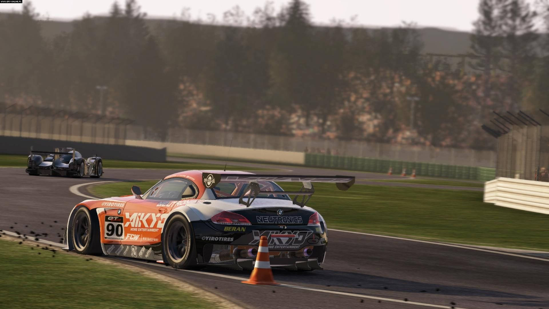 Project Cars 4K 宝马 Z4 模型 壁紙 — 一輛鮮橙色賽車，號碼90，高速駛過彎道，經過一個橙色雪糕筒，遠處有另一輛車。