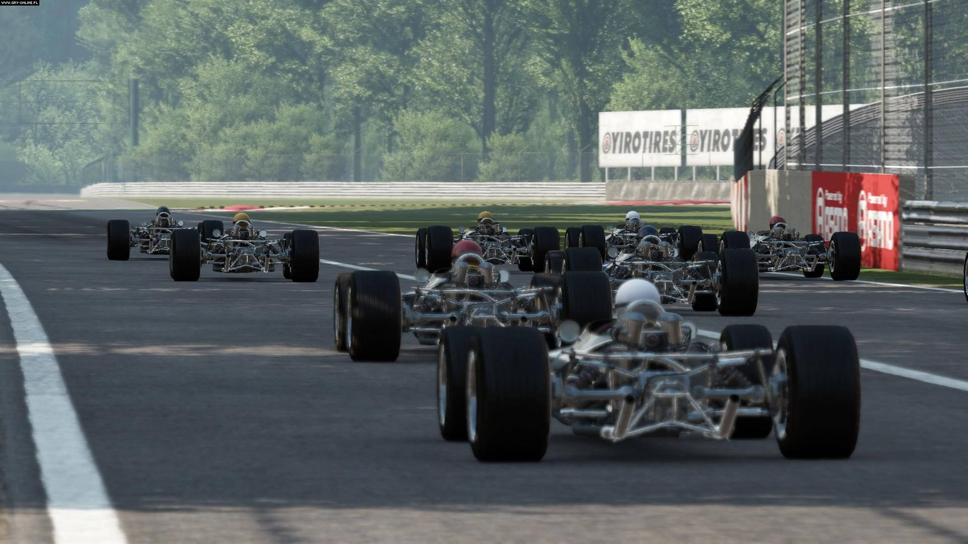 Project Cars 4K 燃燒賽道激情 壁紙 — 一隊開輪賽車卡丁車沿著陽光明媚的瀝青賽道疾馳，賽道兩旁綠樹成蔭，並設有品牌護欄。