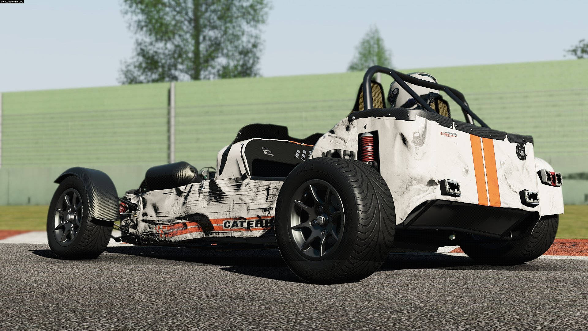 Project Cars 4K 破損車 壁紙 — 一輛白色和橙色的賽車，帶有黑色點綴，停在賽道上，背景有綠色護欄和樹木，天空晴朗。