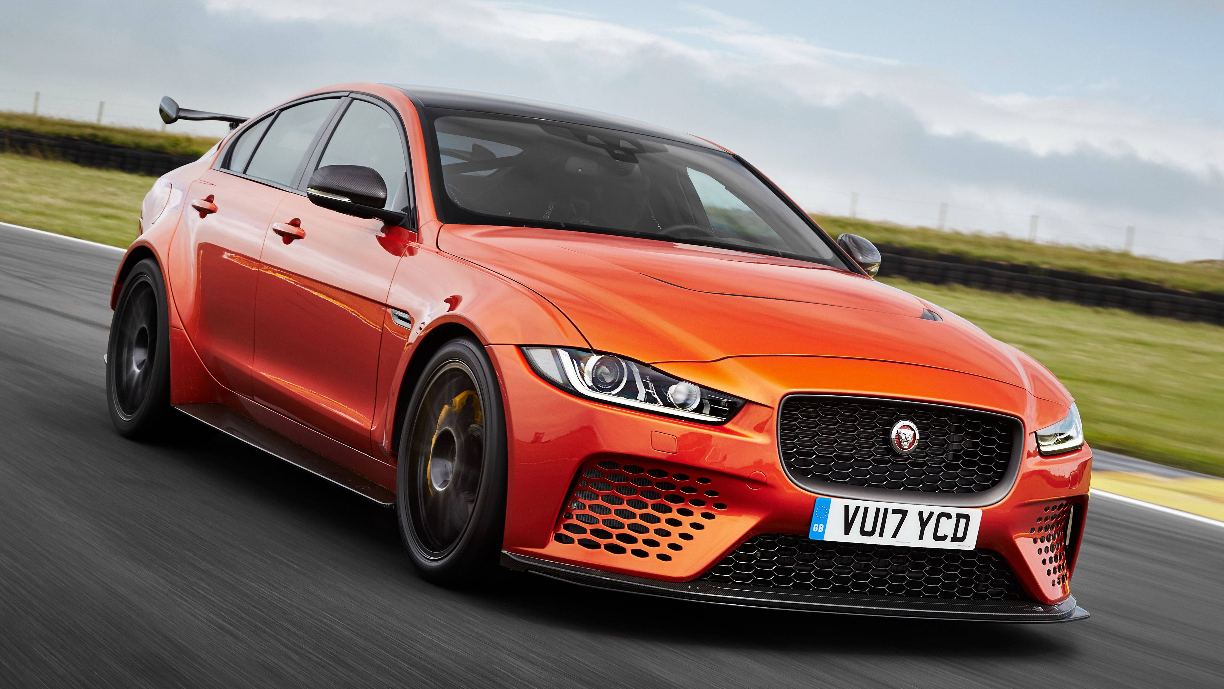 Project Cars 4K 高速競賽 壁紙 — 一輛充滿活力的橙色Jaguar XE SV Project 8在賽道上疾馳，背景是模糊的綠色草地和多雲的天空。