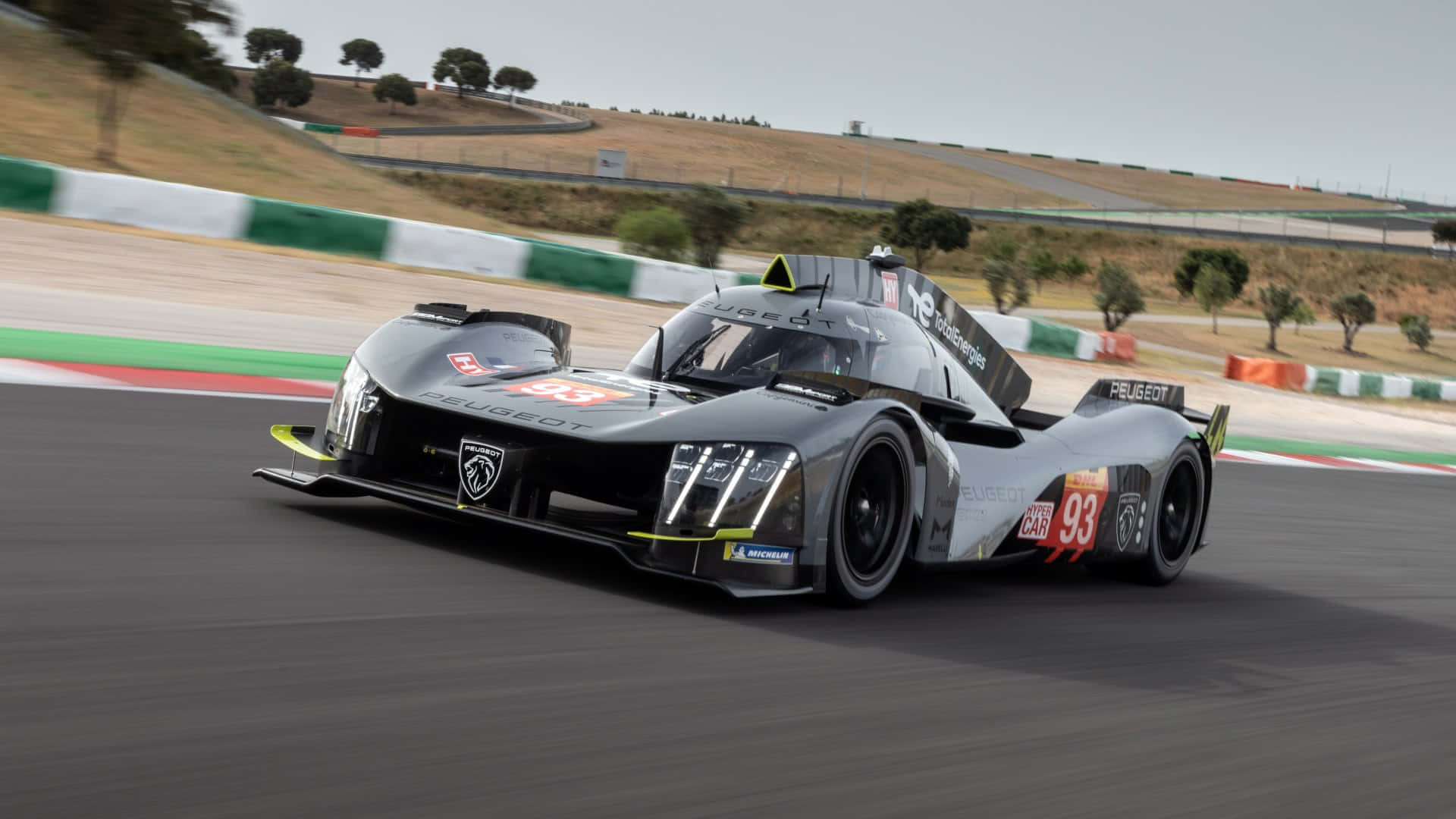 Project Cars 白色 Peugeot 9X8 高清背景 壁紙 — 一輛流線型的標緻LMP1賽車在陽光普照的賽道上疾馳，帶有動態模糊和綠白相間的護欄。