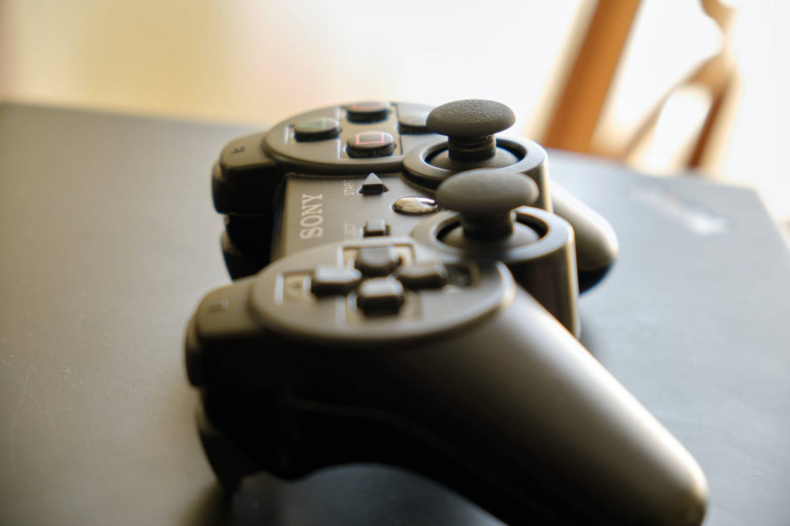 黑色PS3控制器 壁紙 — 黑色Sony PlayStation 3手掣嘅特寫，放喺黑暗表面，配以柔和溫暖嘅燈光。