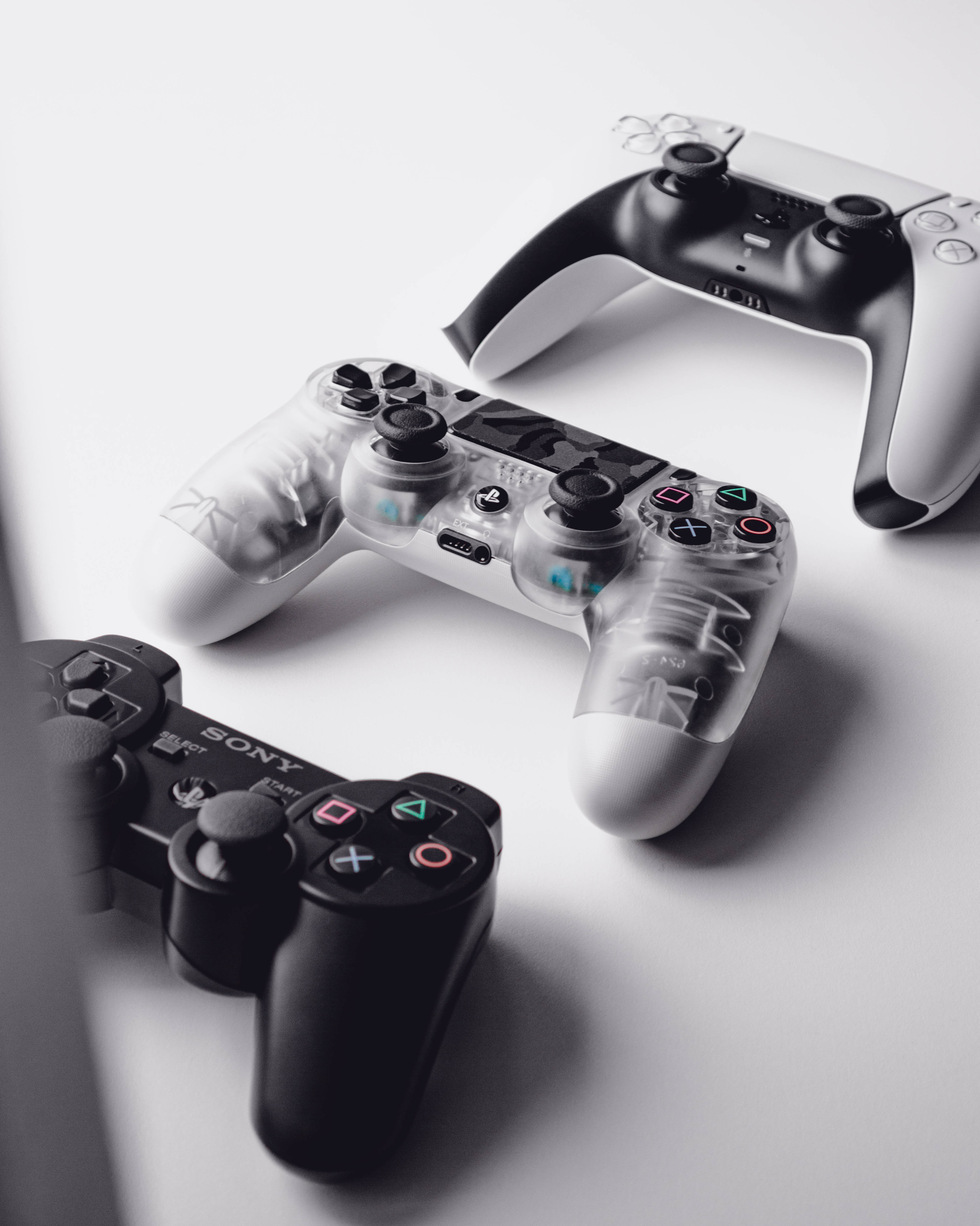 三款不同 PS3 控制器 壁紙 — 三個Sony PlayStation控制器，採用黑色半透明和白色設計，排列在簡約的白色表面上。