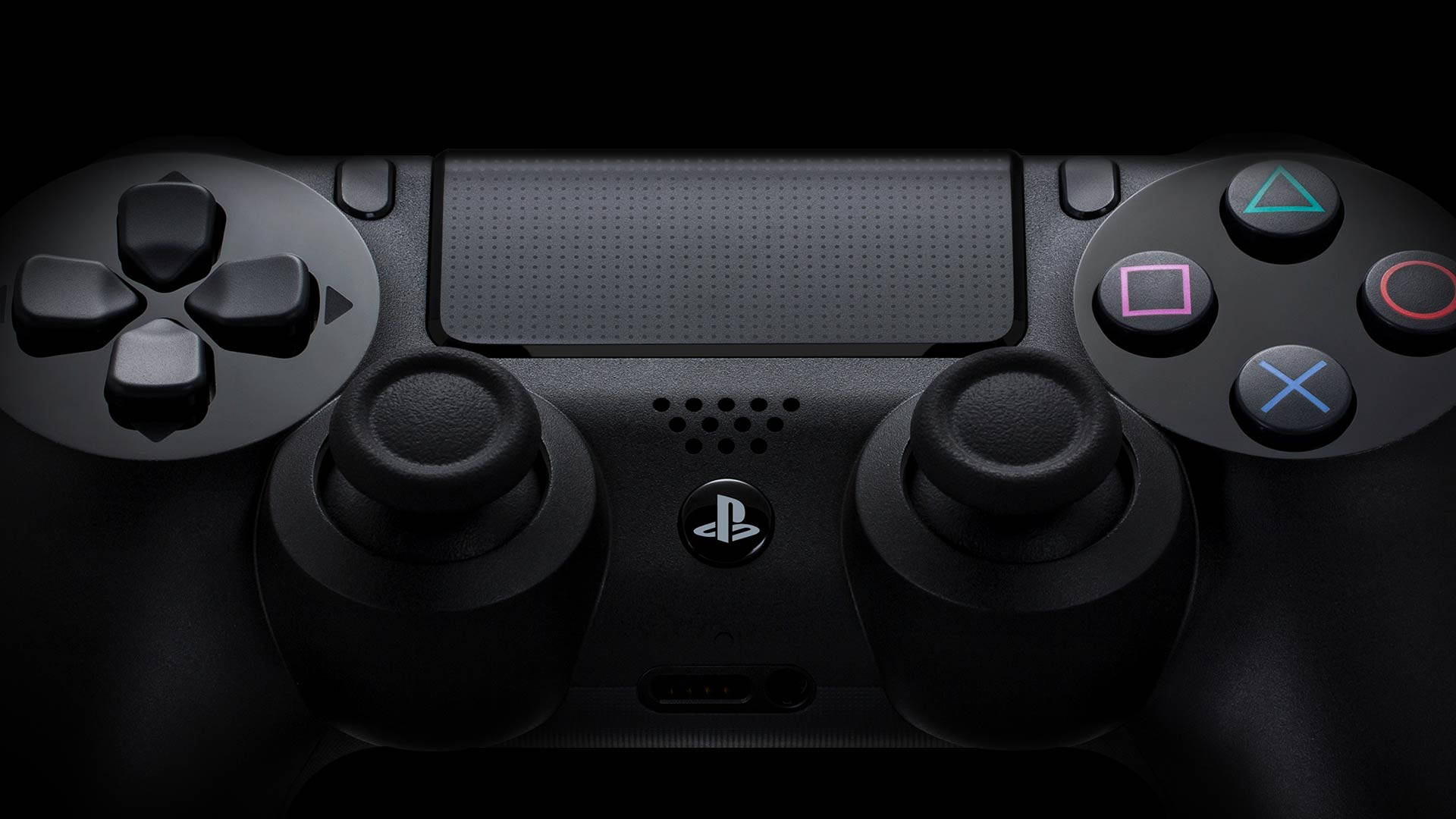 PS4控制器特寫 壁紙 — 黑色PlayStation手掣特寫，帶有發光彩色按鈕，背景昏暗。