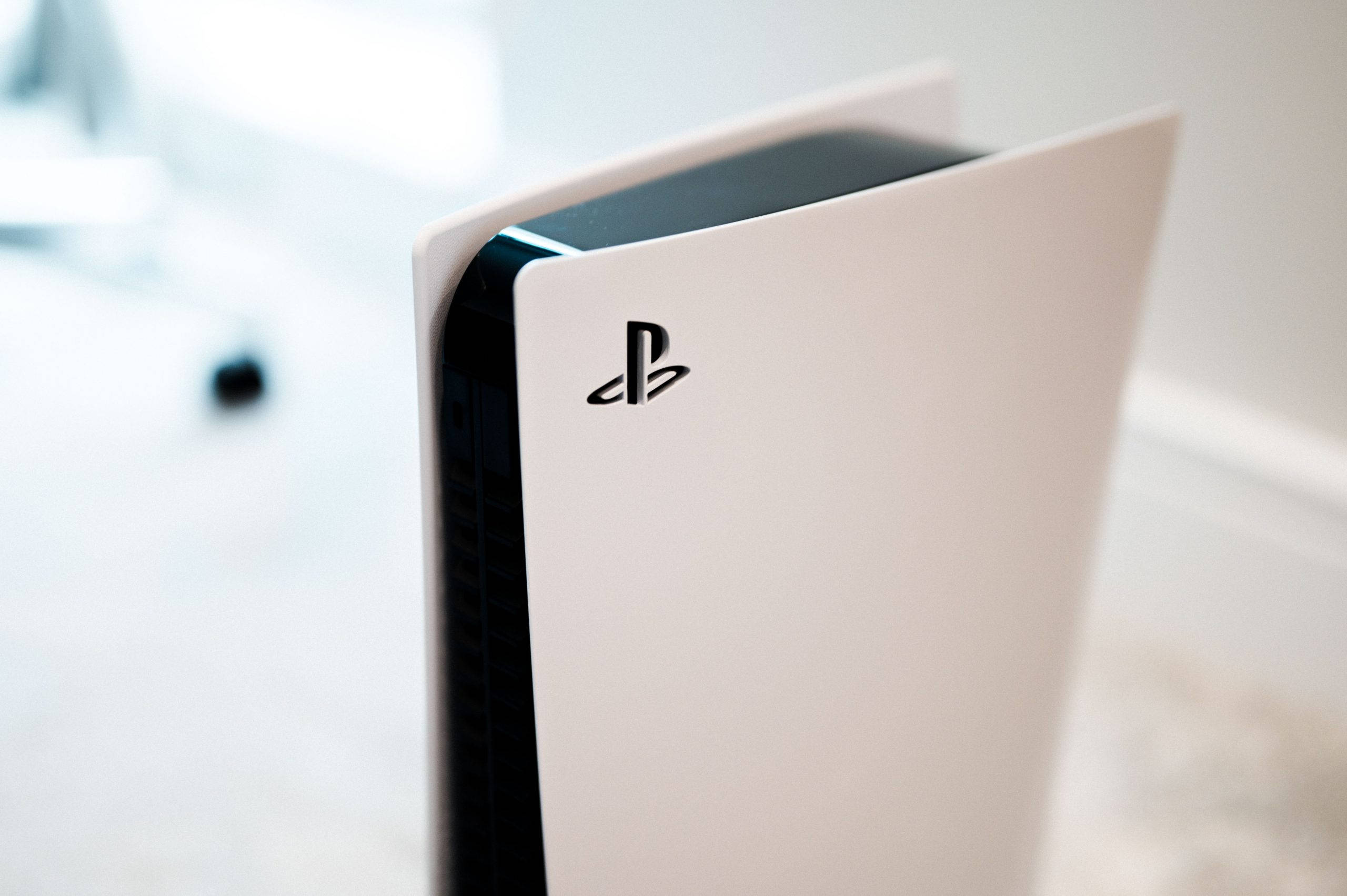 PS5 主機特寫 壁紙 — 白色PlayStation 5主機特寫，帶有黑色點綴和標誌，在明亮的室內環境中直立放置。