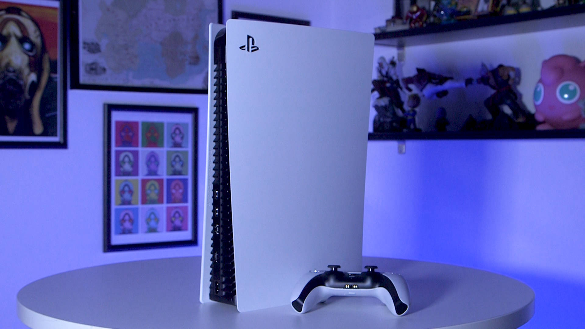 白色PlayStation 5主機和手掣在桌上，配有藍色燈光和普普藝術海報。