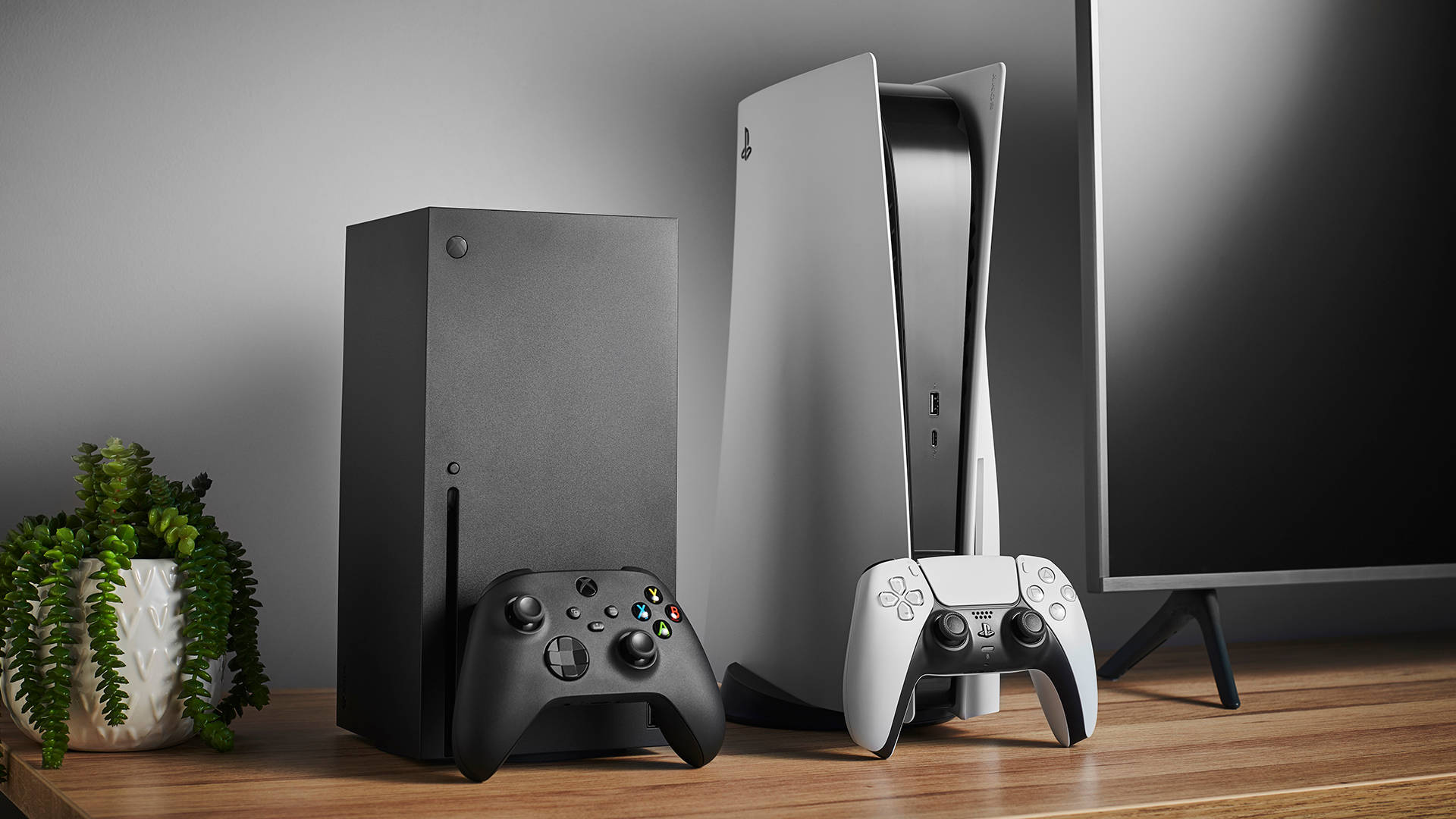 PS5與Xbox Series X 壁紙 — 兩部現代遊戲主機Xbox Series X和PlayStation 5並排放在木架上，旁邊有控制器和盆栽植物。