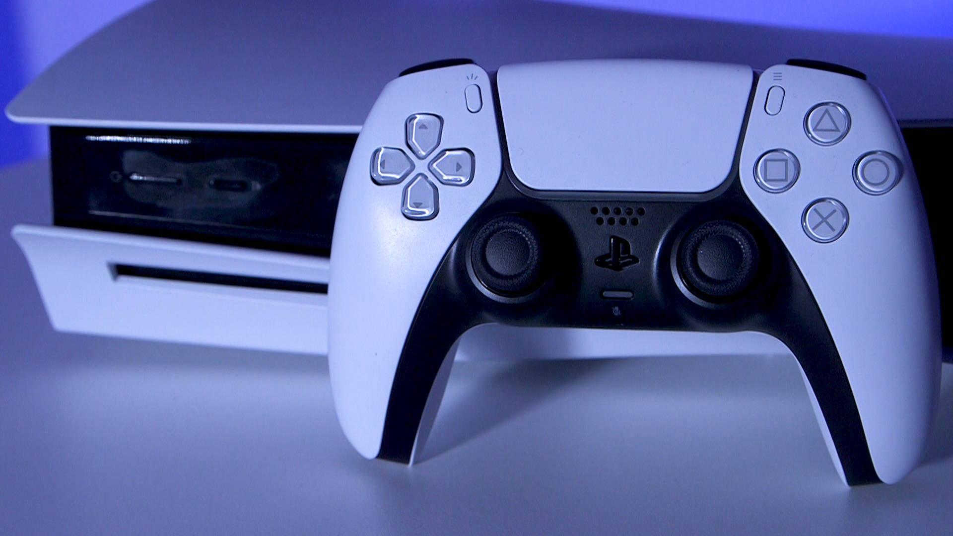 PS5遊戲控制器美學 壁紙 — 一個白色PlayStation 5手掣放在主機前，在冷藍色燈光下。