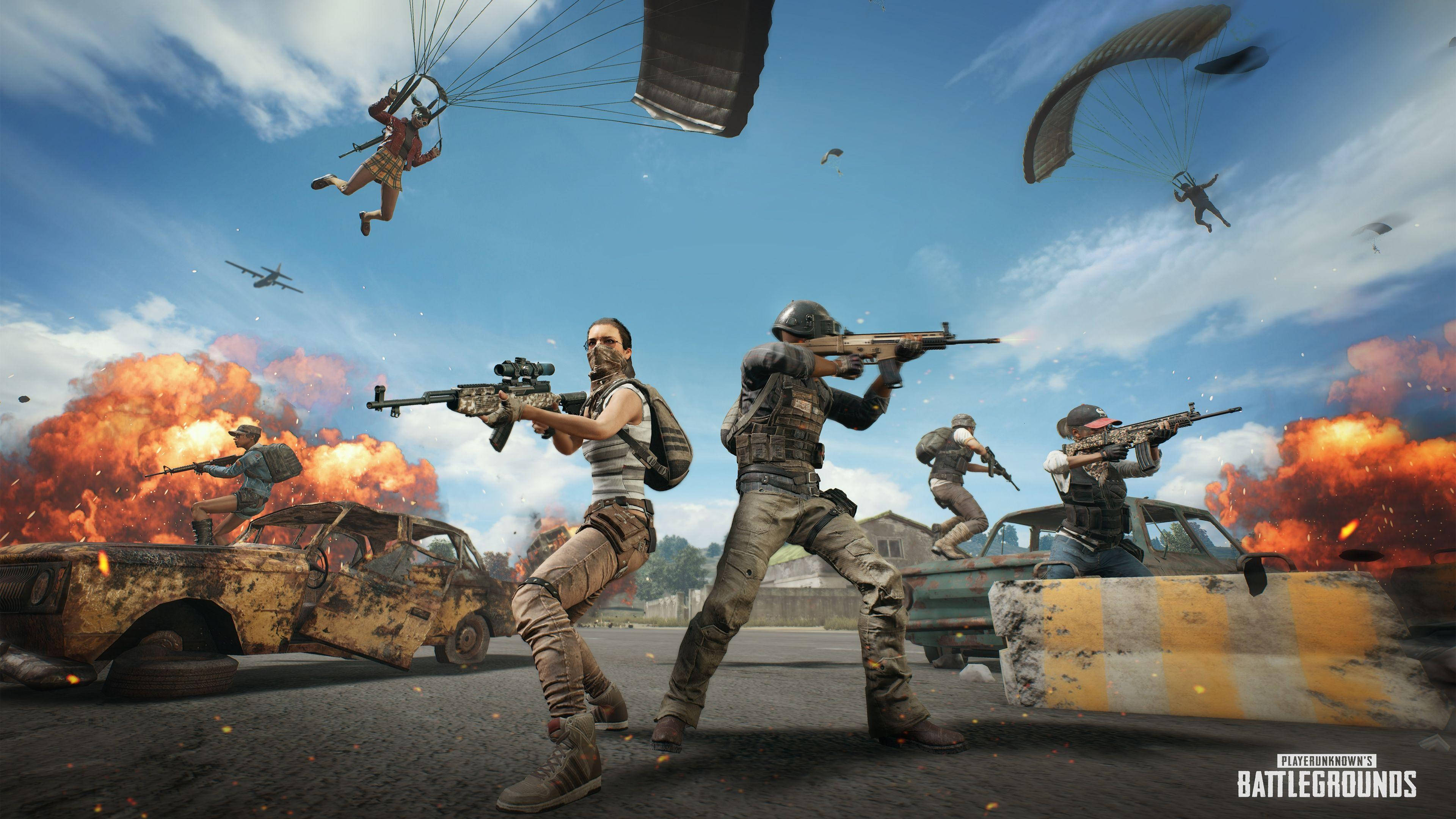 PUBG Lite 炎熱大逃殺戰鬥場景 壁紙 — 身穿戰鬥裝備的士兵在爆炸和燃燒的汽車中開火，而傘兵在混亂的大逃殺場景中降落。