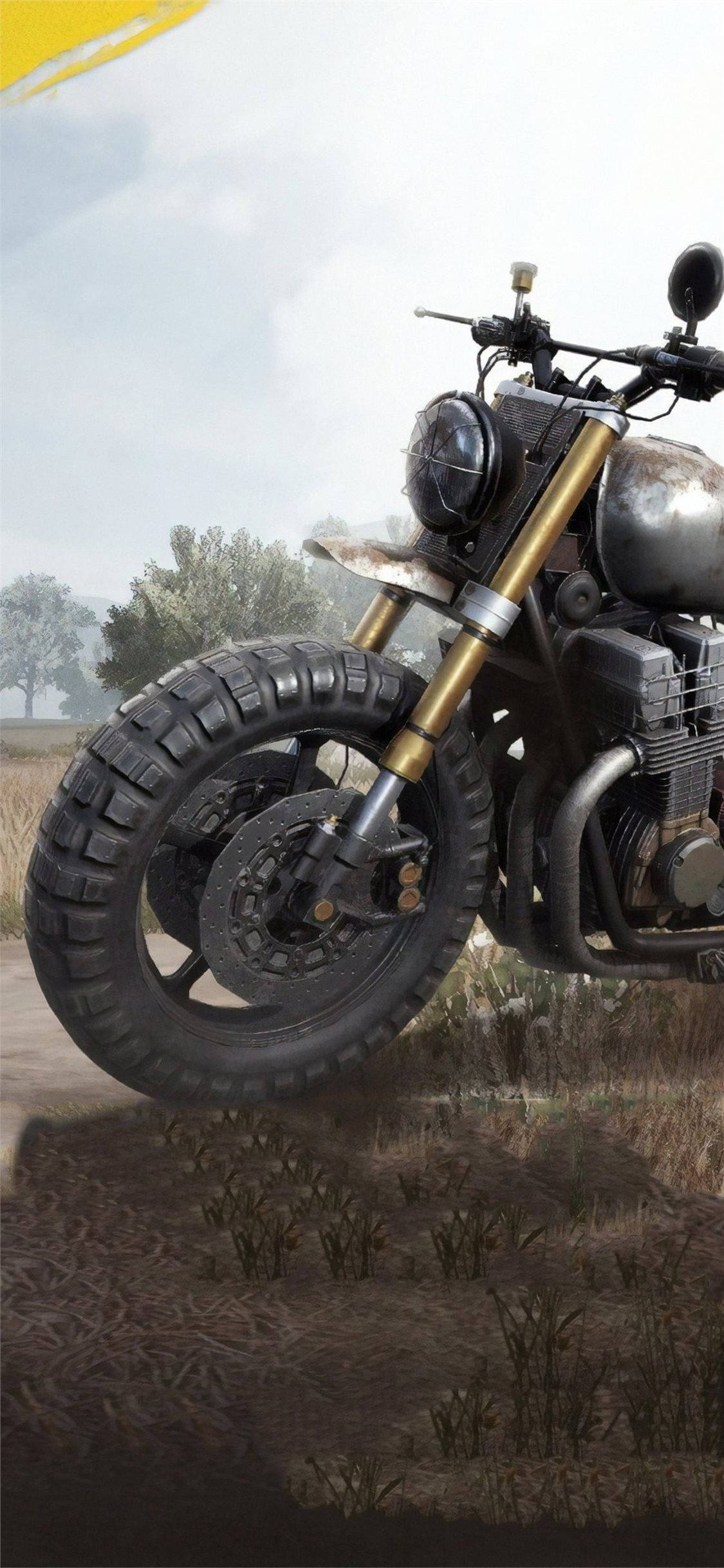 PUBG遊戲4K自行車圖像 壁紙 — 一輛堅固的越野電單車，配備金色前叉和越野輪胎，停在乾燥的草地上，天空多雲。