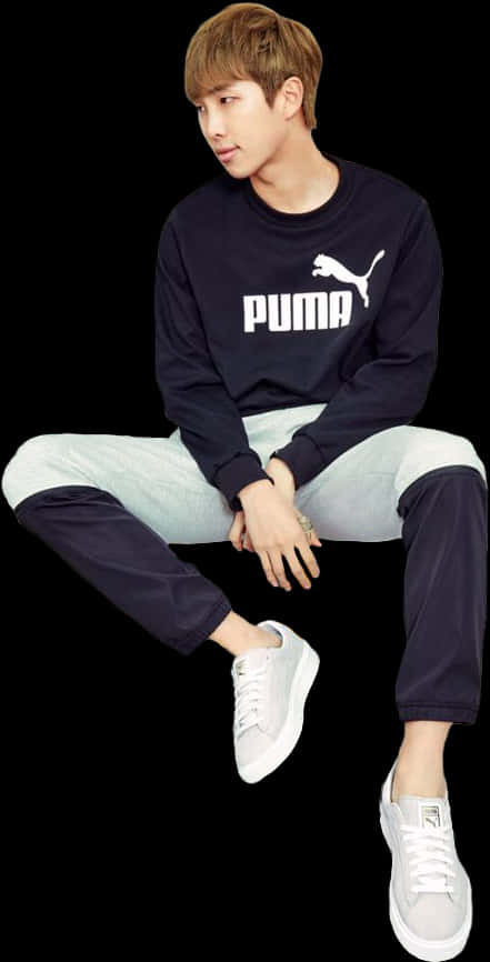 休閒PUMA穿搭坐姿 壁紙 — 一名身穿海軍藍Puma運動衫和雙色褲的年輕男子，盤腿坐在黑色背景前，穿著白色運動鞋。
