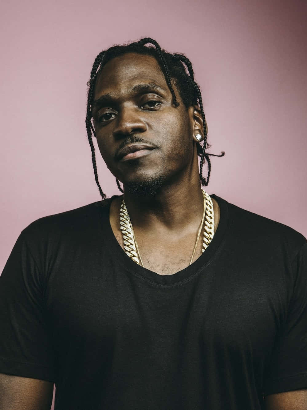 Pusha T 粉紅背景肖像 壁紙 — 一個辮子頭髮、戴著金鏈的男人，在柔和的粉紅色工作室背景下自信地凝視著。