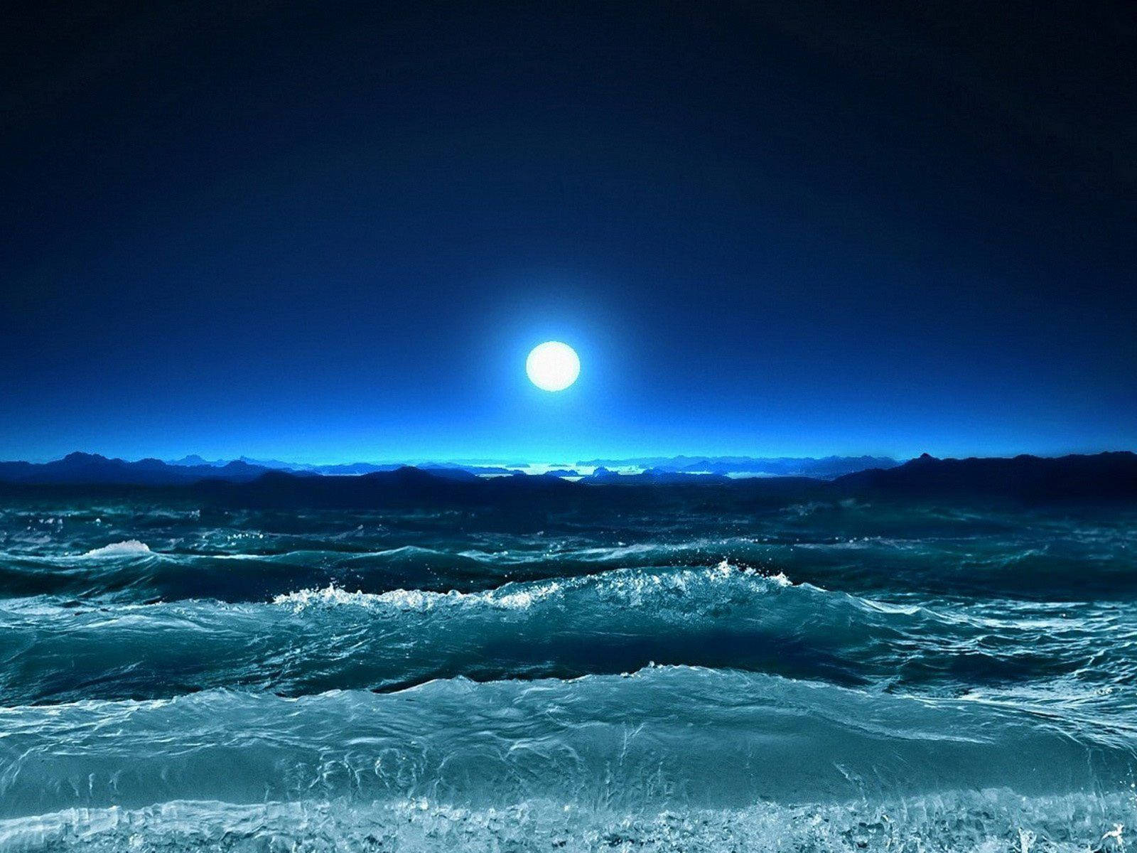 QHD 海洋月升 壁紙 — 一輪明亮的滿月在深靛藍色的夜空下，在波濤洶湧的海洋上投下空靈的光芒。