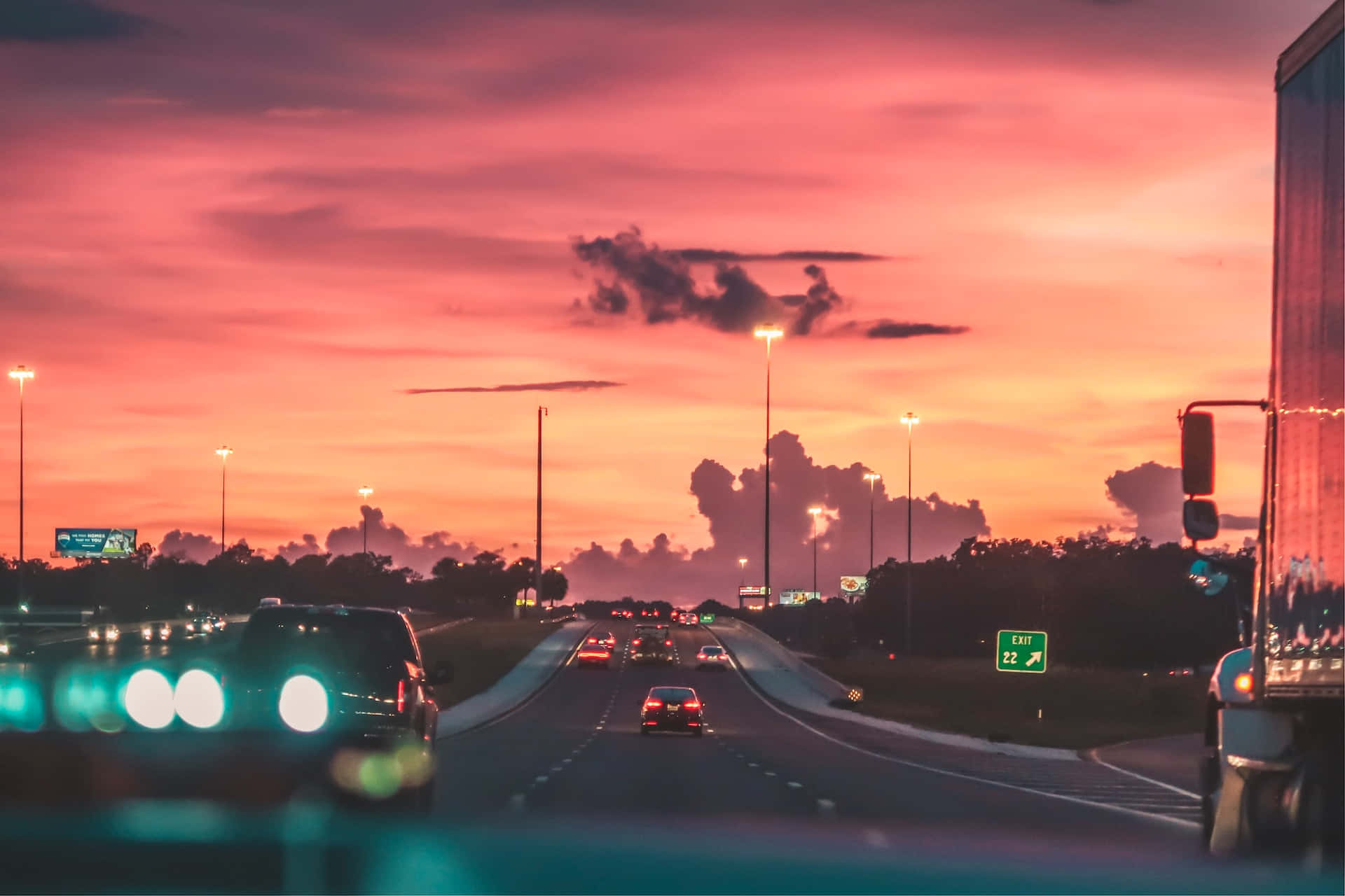 Sunset Drive 桌布 壁紙 — 汽車在高速公路上行駛，天空呈現火熱的粉紅色和橙色日落，伴隨著戲劇性的雲彩。