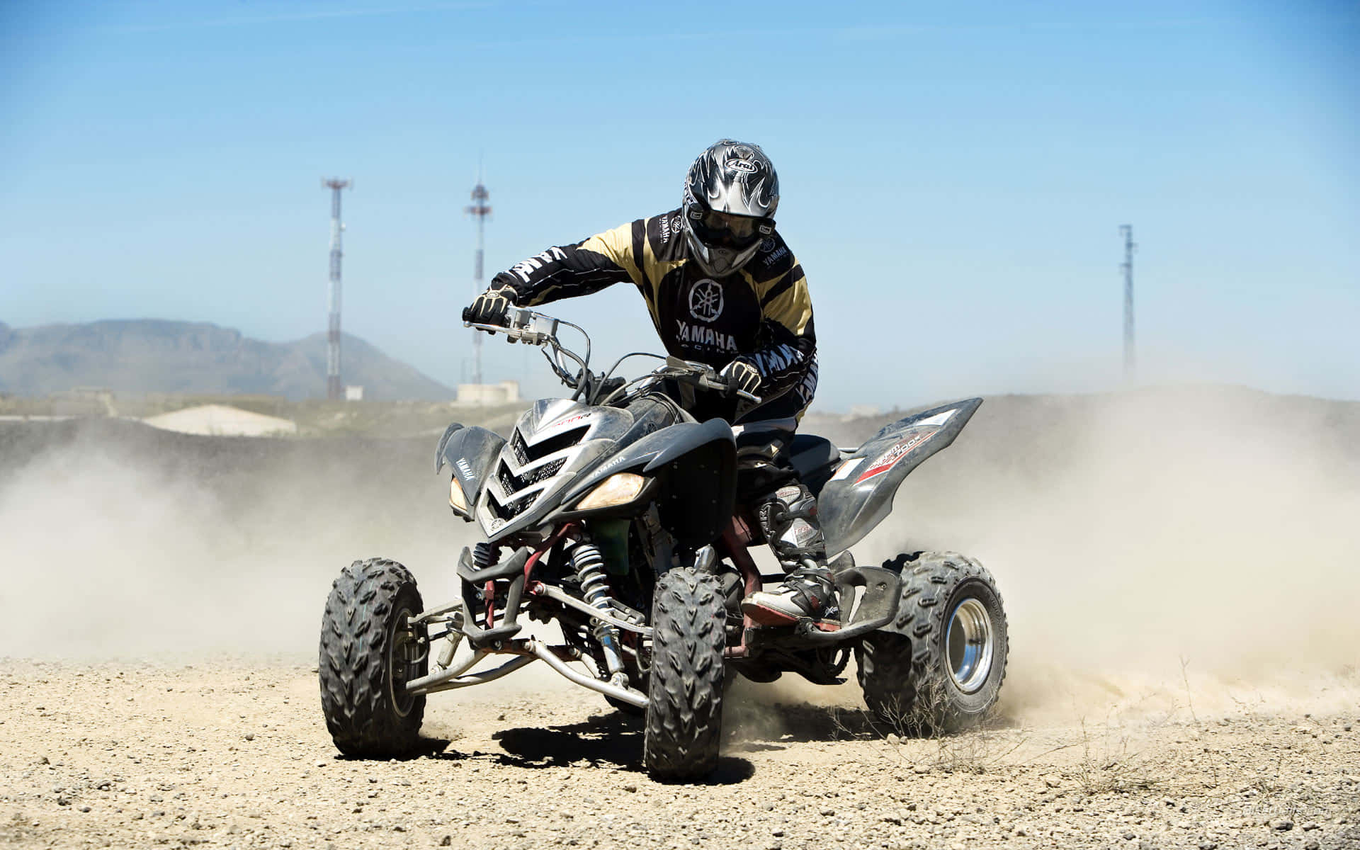  壁紙 — 一名全副裝備的騎手駕駛Yamaha ATV穿越塵土飛揚的沙漠地形，在清澈的藍天下揚起沙塵雲。