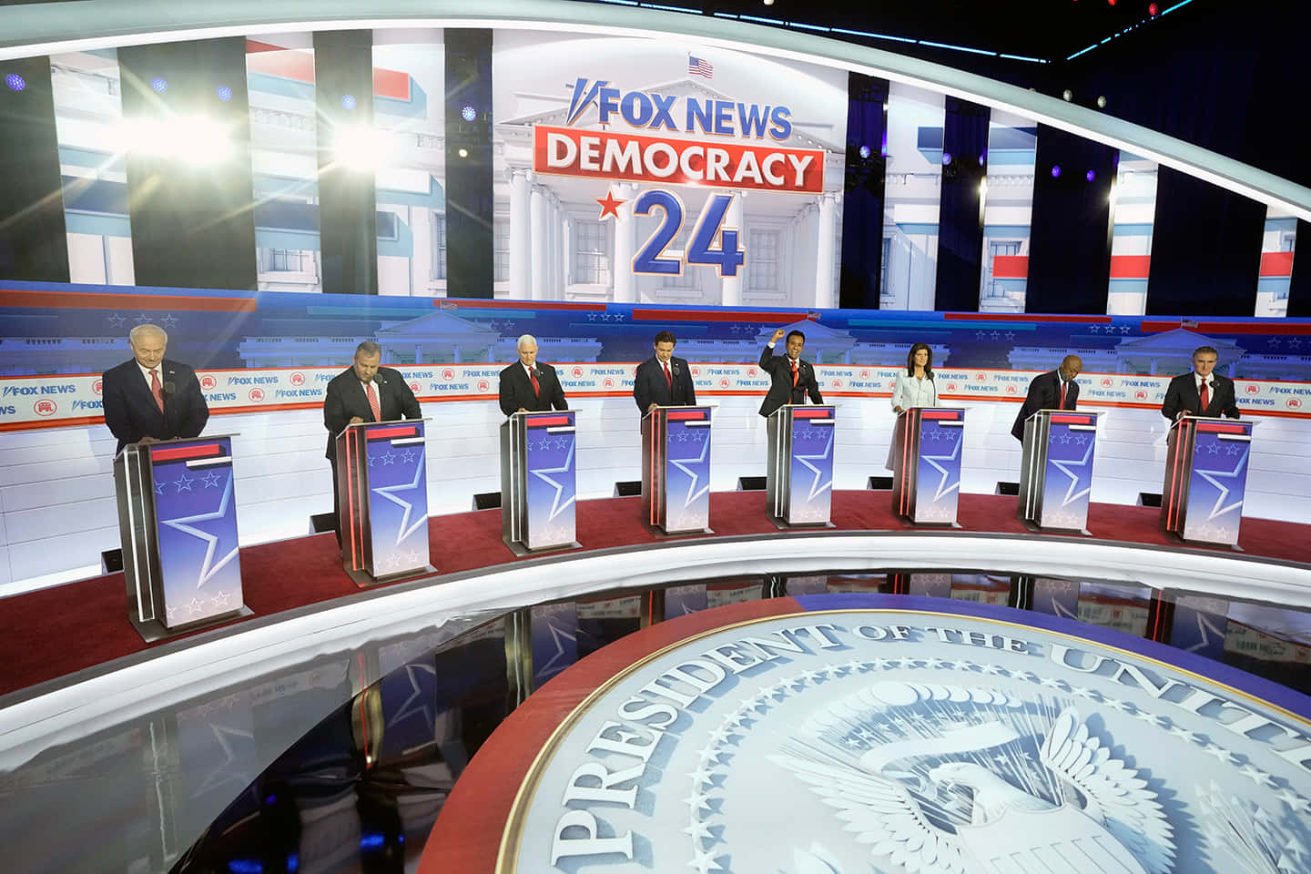  壁紙 — 七位候選人站在帶有Fox News Democracy 24和總統印章的弧形舞台講台上。