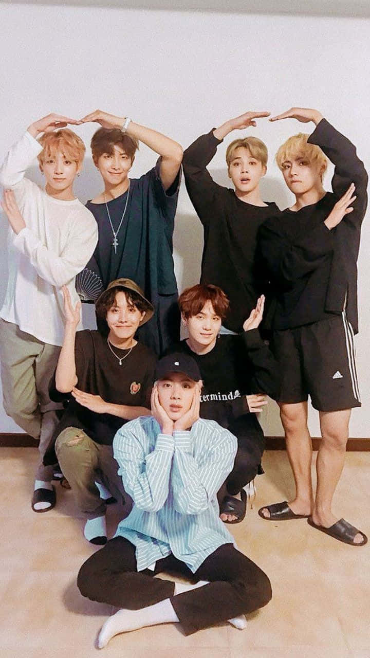 BTS男孩團體合照比心 壁紙 — 七位年輕男子在室內俏皮地擺姿勢，雙手在頭頂比出心形。