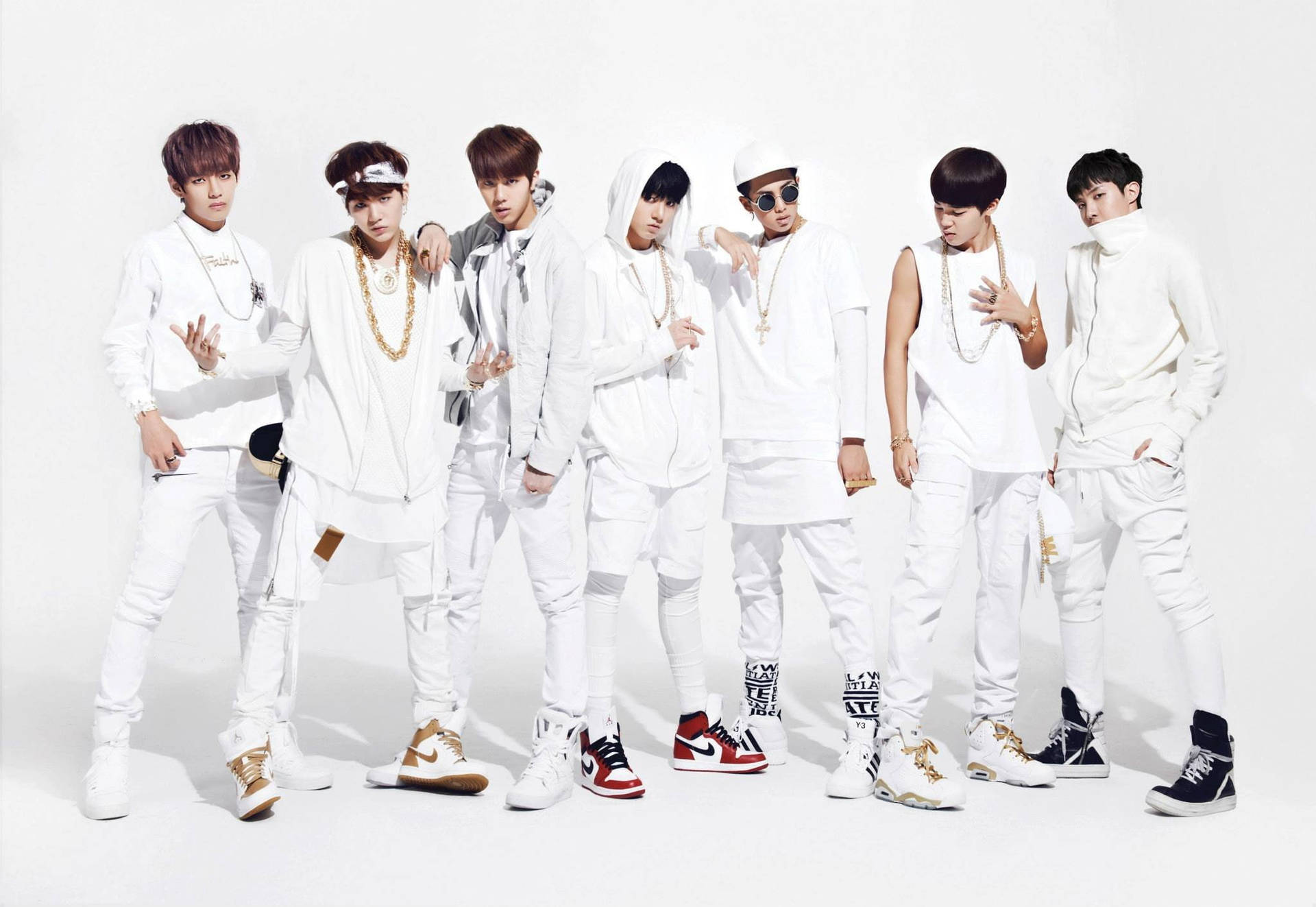 O!RUL8,2 酷炫BTS筆電壁紙 壁紙 — 七位時尚年輕男士身穿白色服裝，佩戴金色飾品和色彩繽紛的運動鞋，在純白背景前自信地擺姿勢。