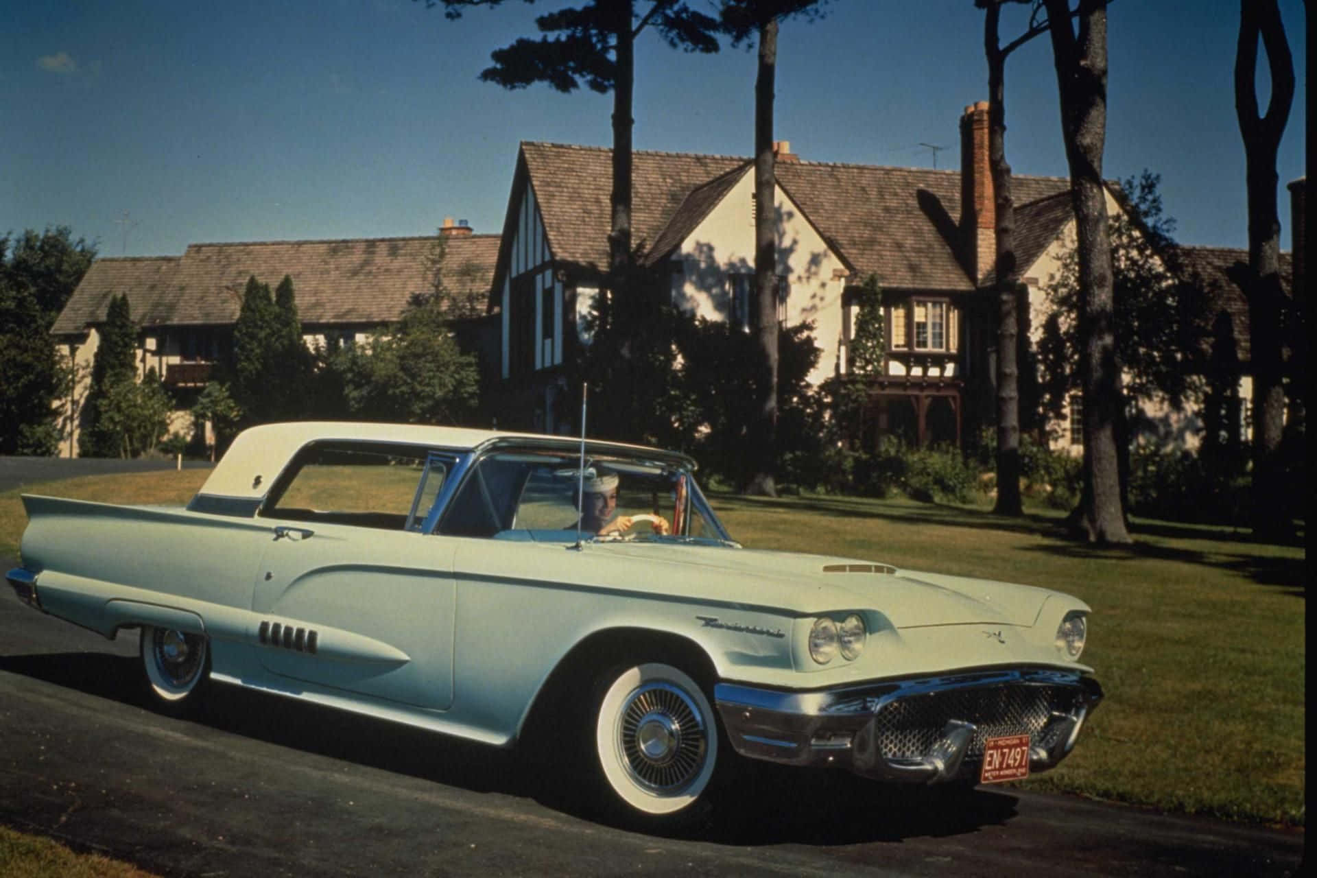 Ford Thunderbird 桌布 壁紙 — 一輛淺藍色1950年代Thunderbird開篷車停泊在都鐸式房屋前的車道上，周圍有樹木和晴朗的藍天。