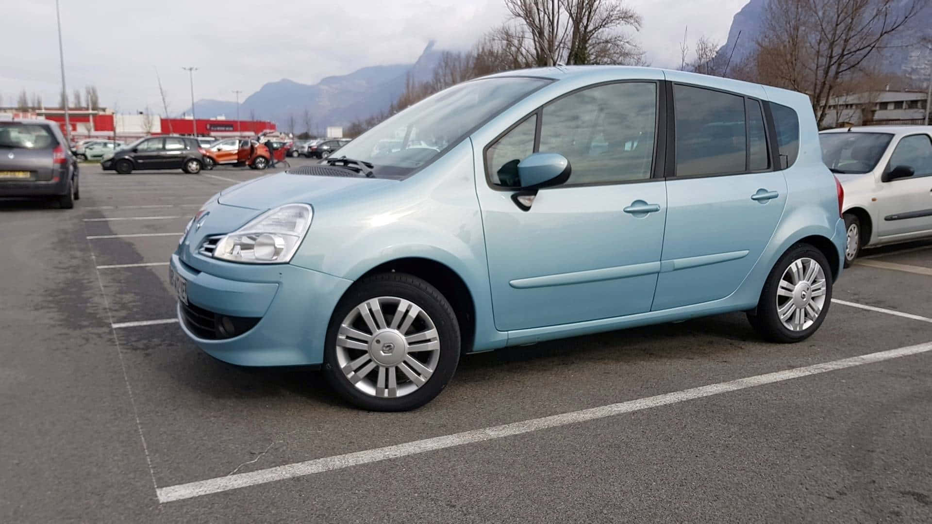 Renault Modus 桌布 壁紙 — 一架淺藍色雷諾Grand Scenic停泊在停車場，背景有山脈，天空多雲。